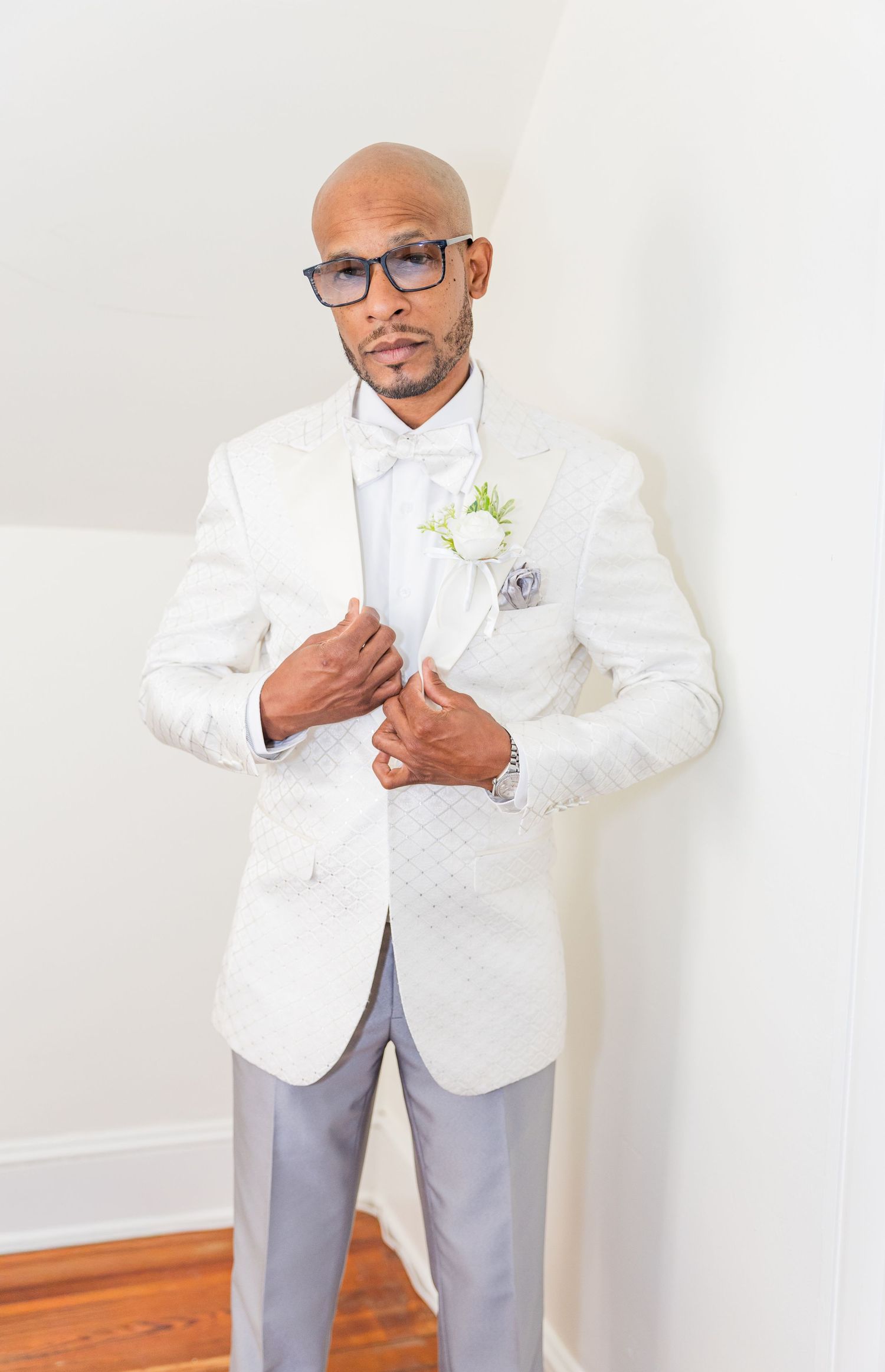 A person in a crisp white blazer and gray pants poses against a light wall.