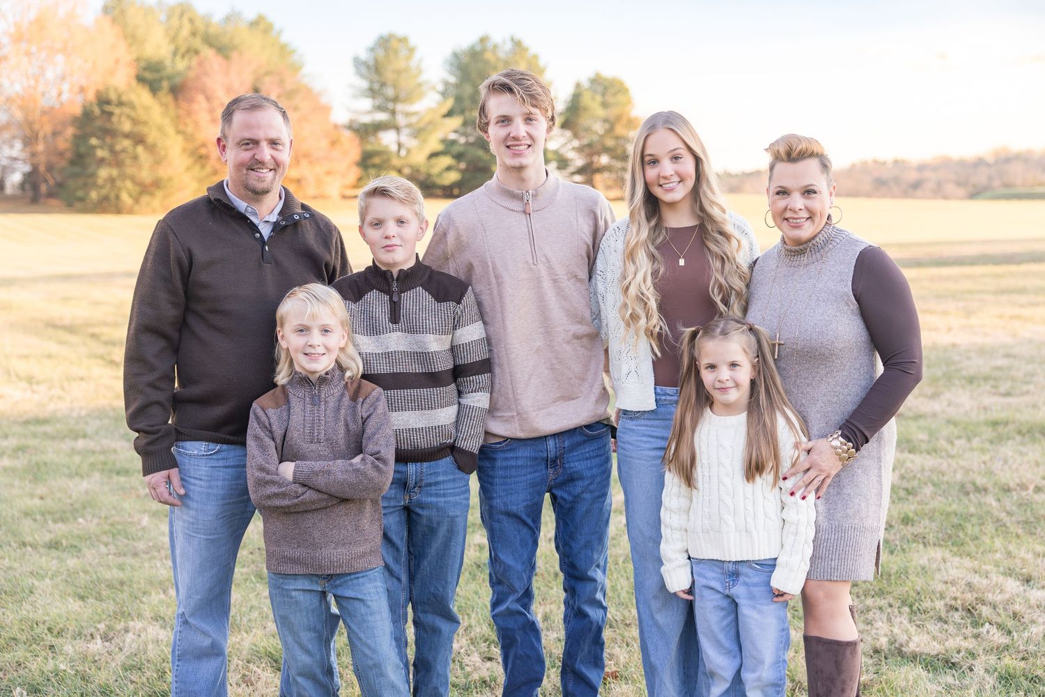 A group of people wearing casual clothing pose together in a grassy field at sunset.