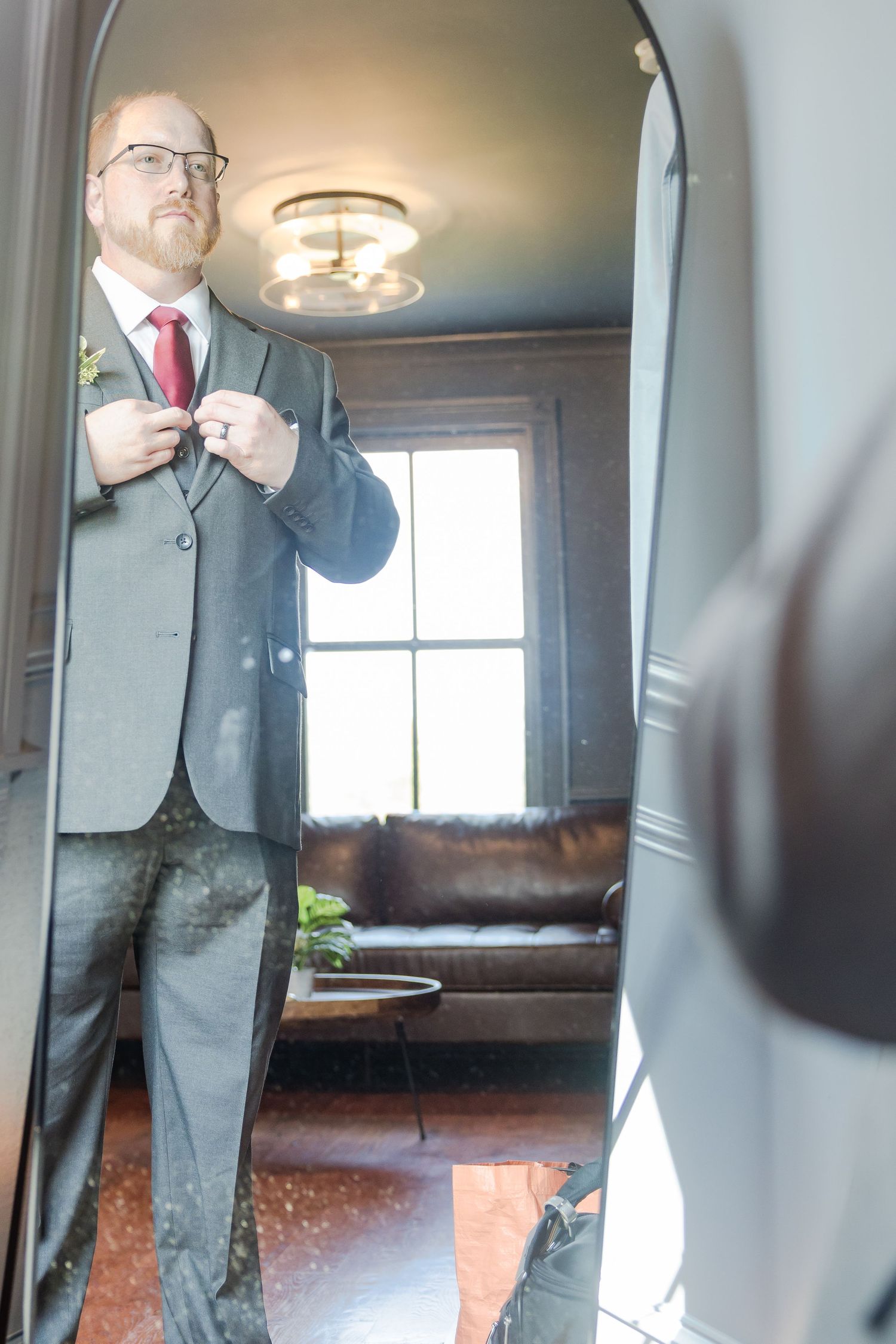 Formal wedding preparation scene showing suit adjustments in an elegant room.