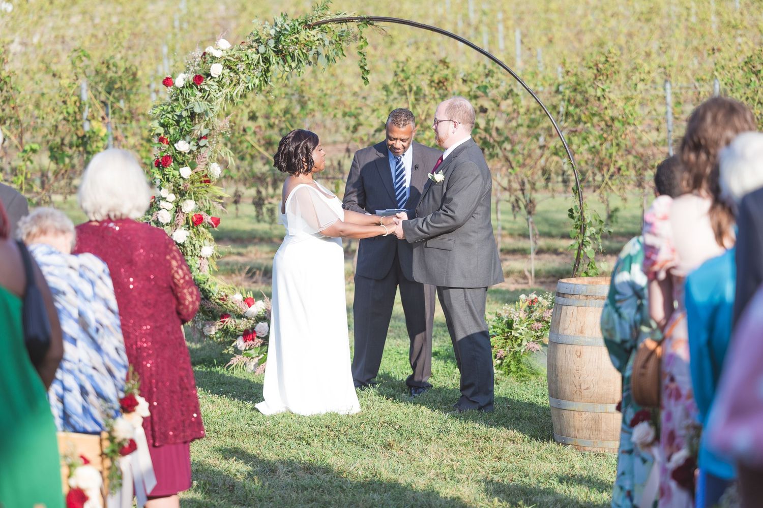 Guests mingle during an outdoor wedding ceremony with rustic barrel decor.