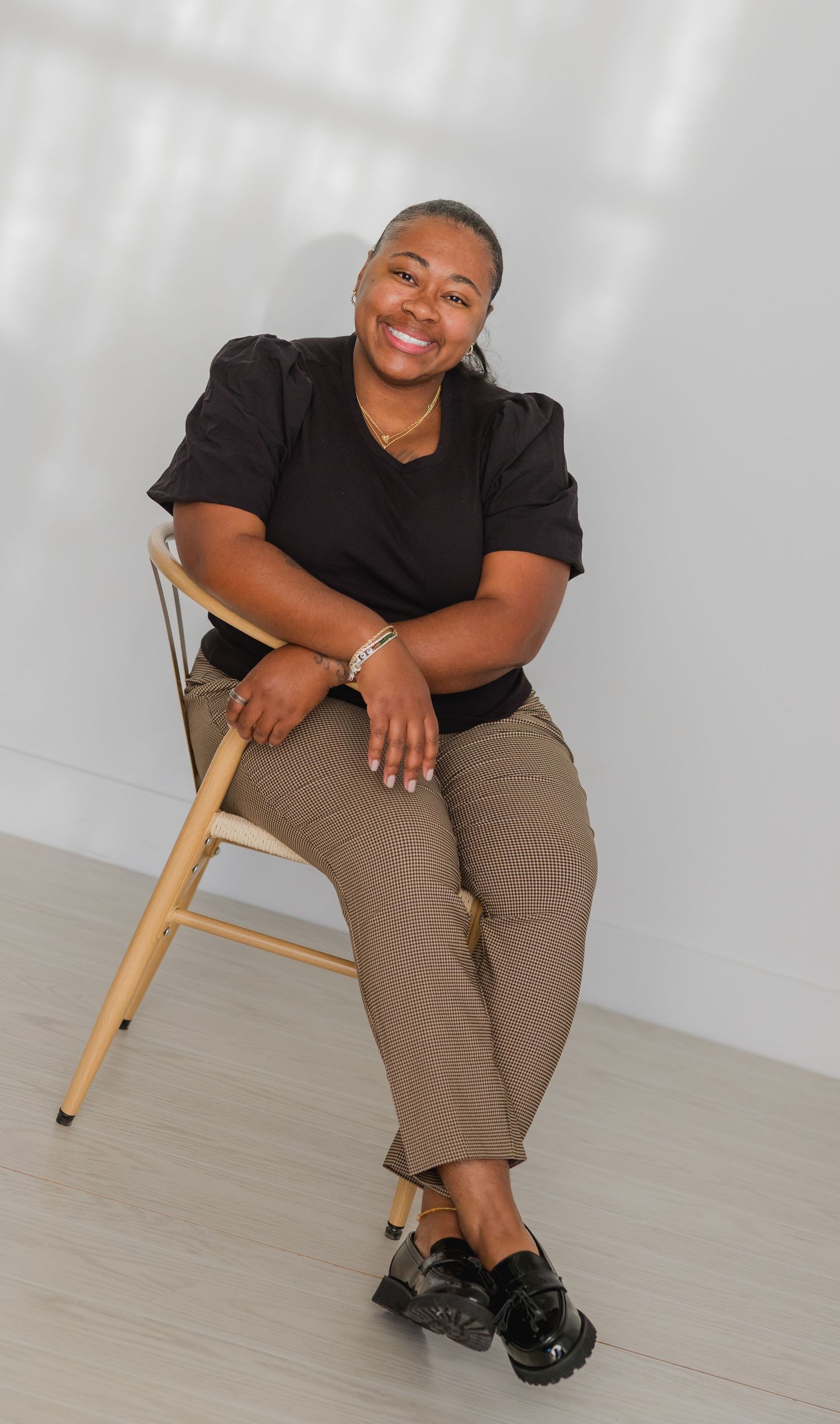 Professional portrait series showing person in black top and khaki pants seated on wooden chair.
