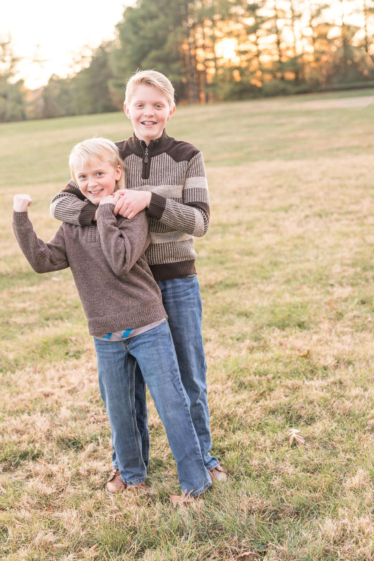 A playful scene in a grassy field at sunset with a child in a brown sweater and jeans being held by an adult.