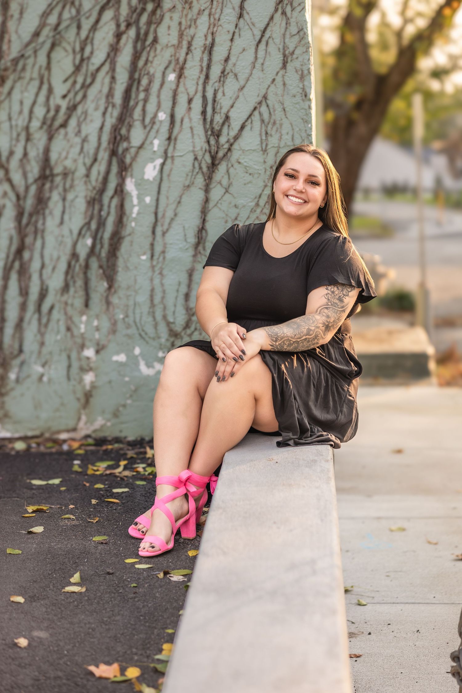 Woman in black dress sitting on concrete ledge wearing bright pink shoes.