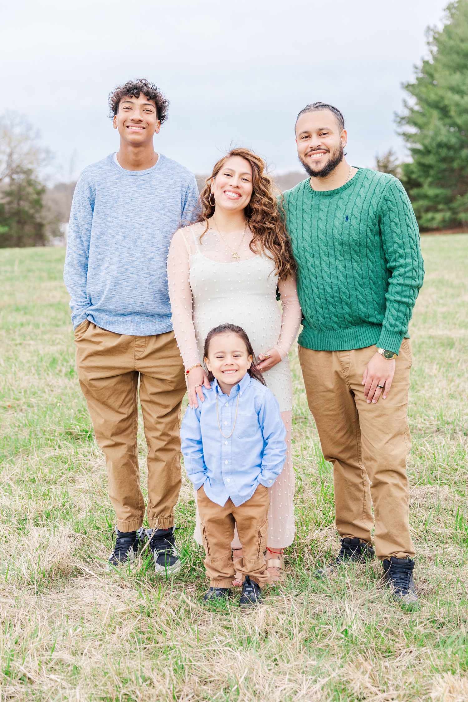 Family wearing coordinated outfits in khaki and blue poses together in a grassy outdoor setting.