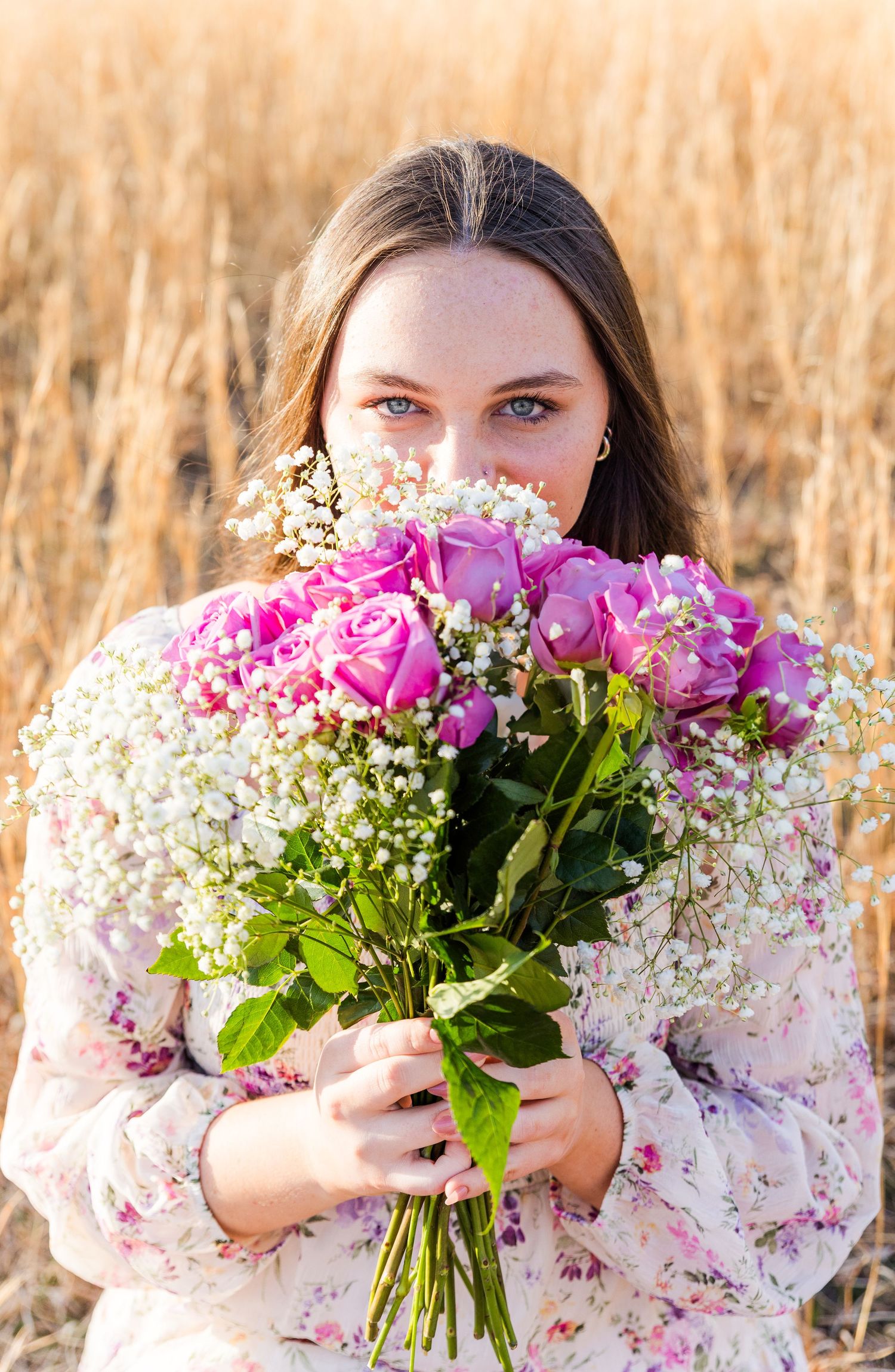 A bouquet of pink roses and baby's breath flowers held in front of a golden field.
