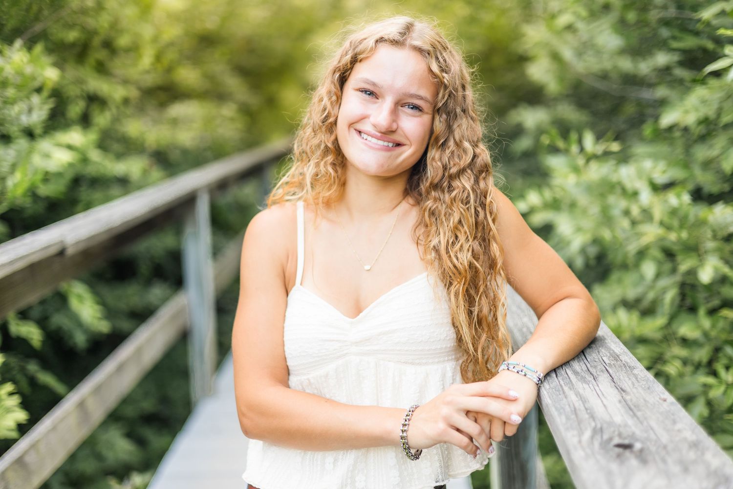 A summer portrait in a white dress on a wooden bridge surrounded by lush greenery.