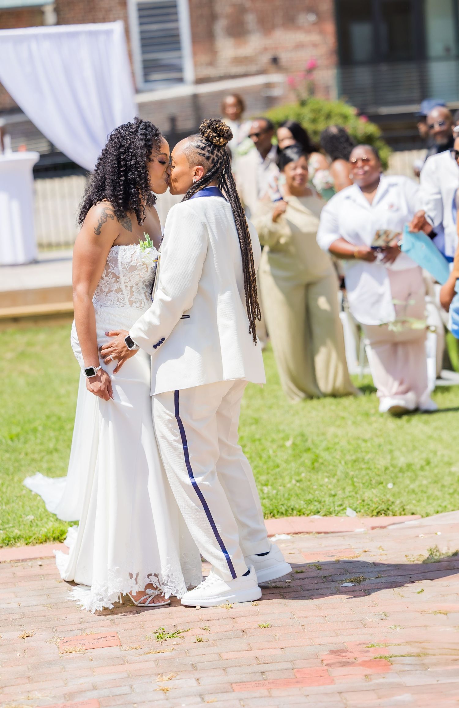 Wedding ceremony on a brick patio with white drapery and guests seated on the lawn.