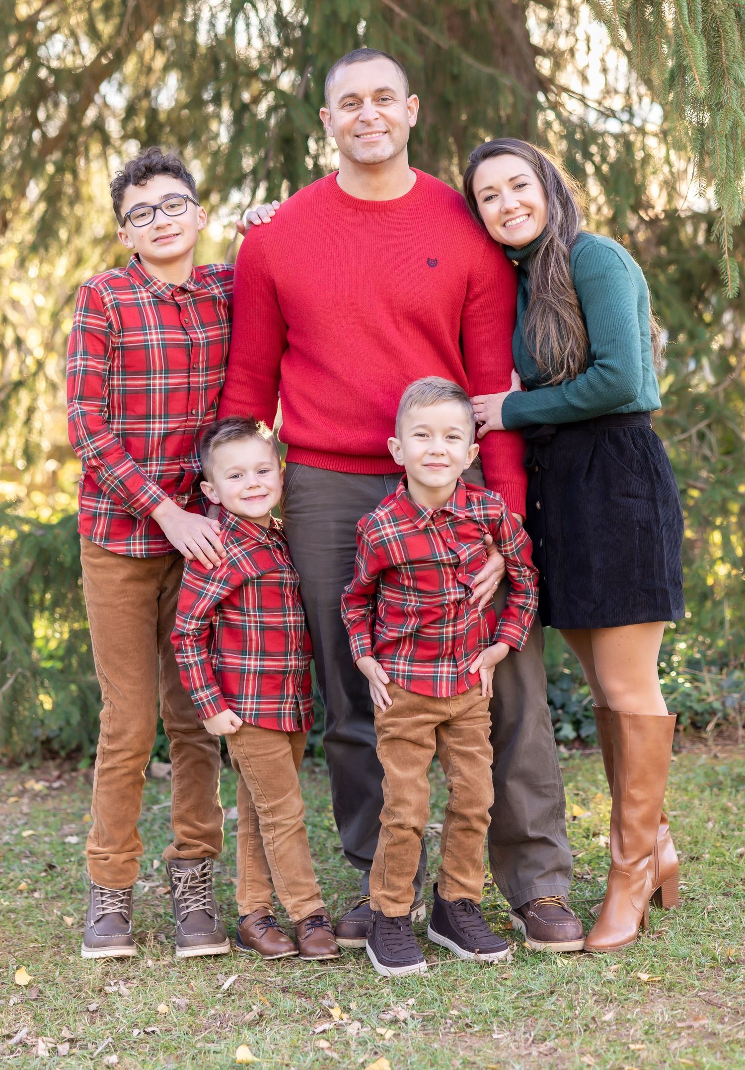 Family wearing coordinated red plaid and solid outfits pose together outdoors.
