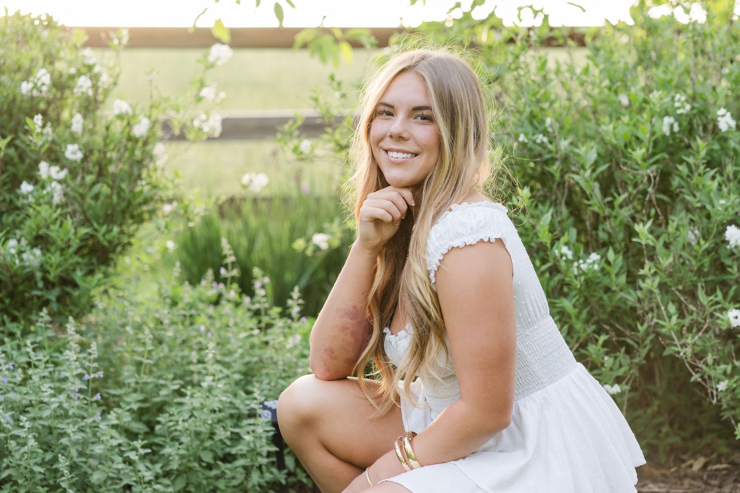 Woman in white dress smiling during outdoor summer photo session.
