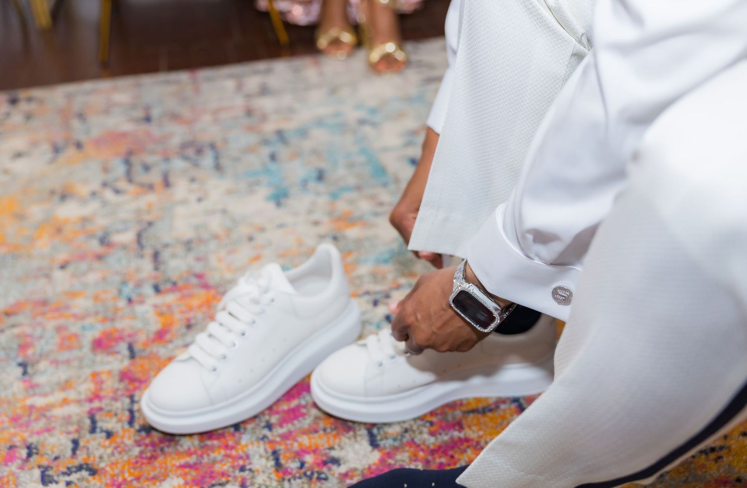 Close-up of white dress shoes on a colorful patterned carpet.