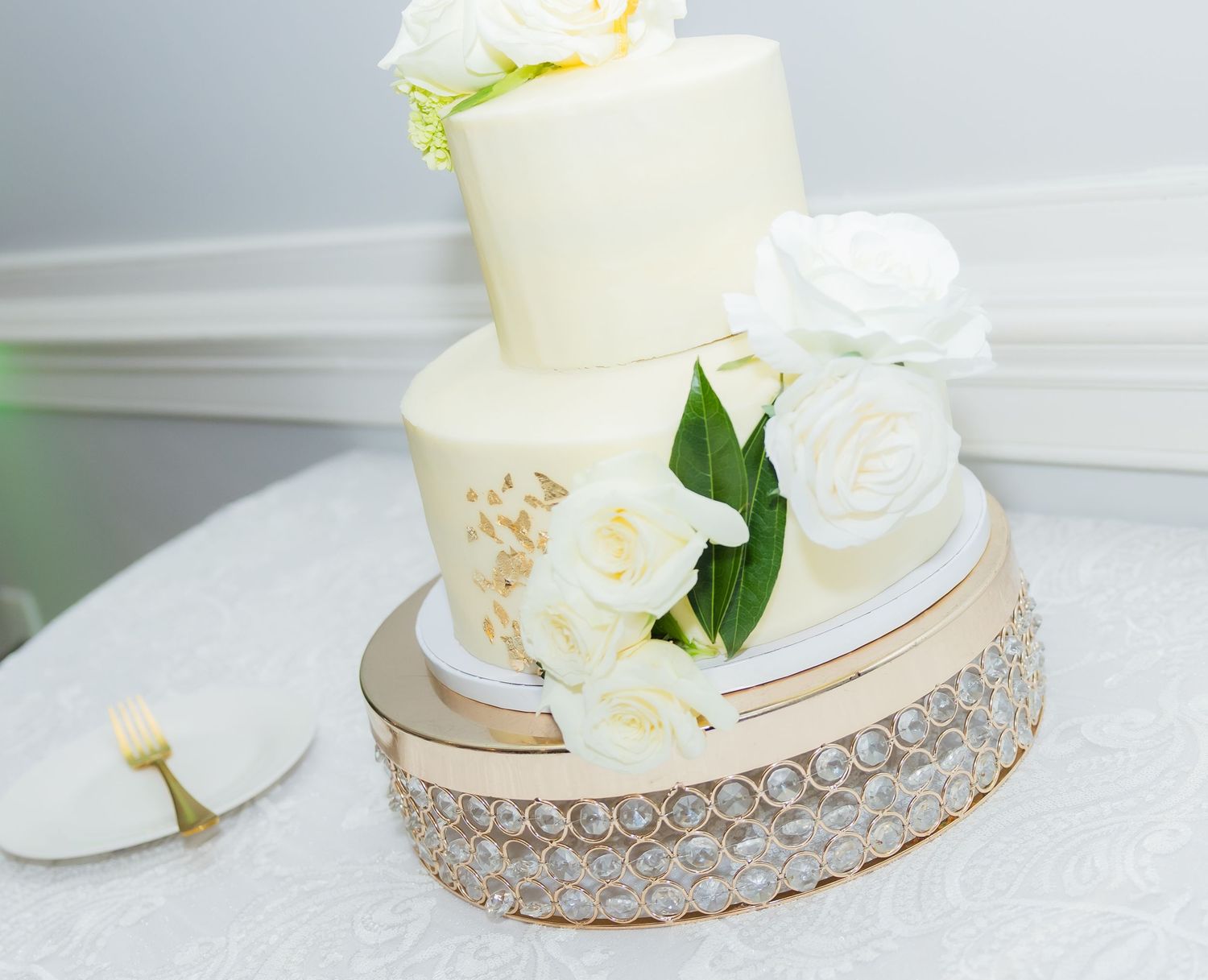 An elegant white wedding cake with floral decorations sits on a crystal-trimmed cake stand.