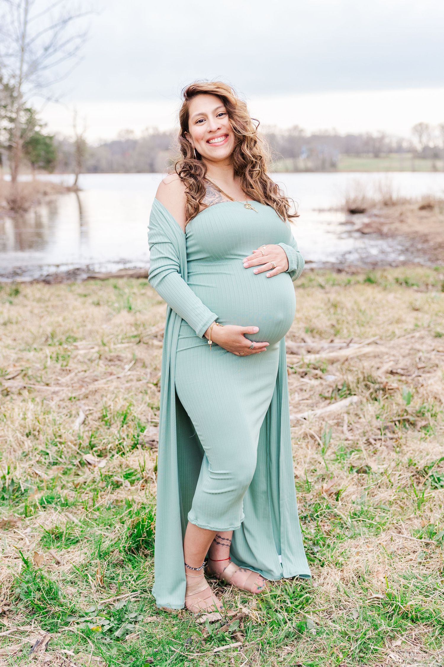 Candid maternity portraits in a mint green dress against a natural lakeside setting.