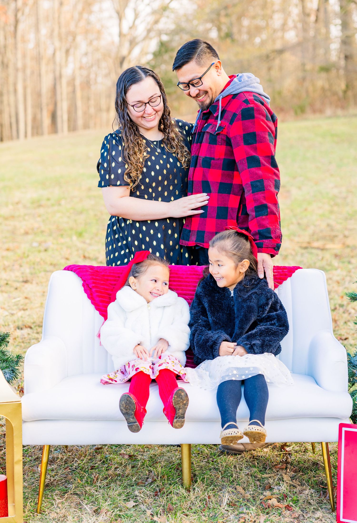 Family members sit together on a white couch outdoors wearing buffalo plaid and festive winter attire.