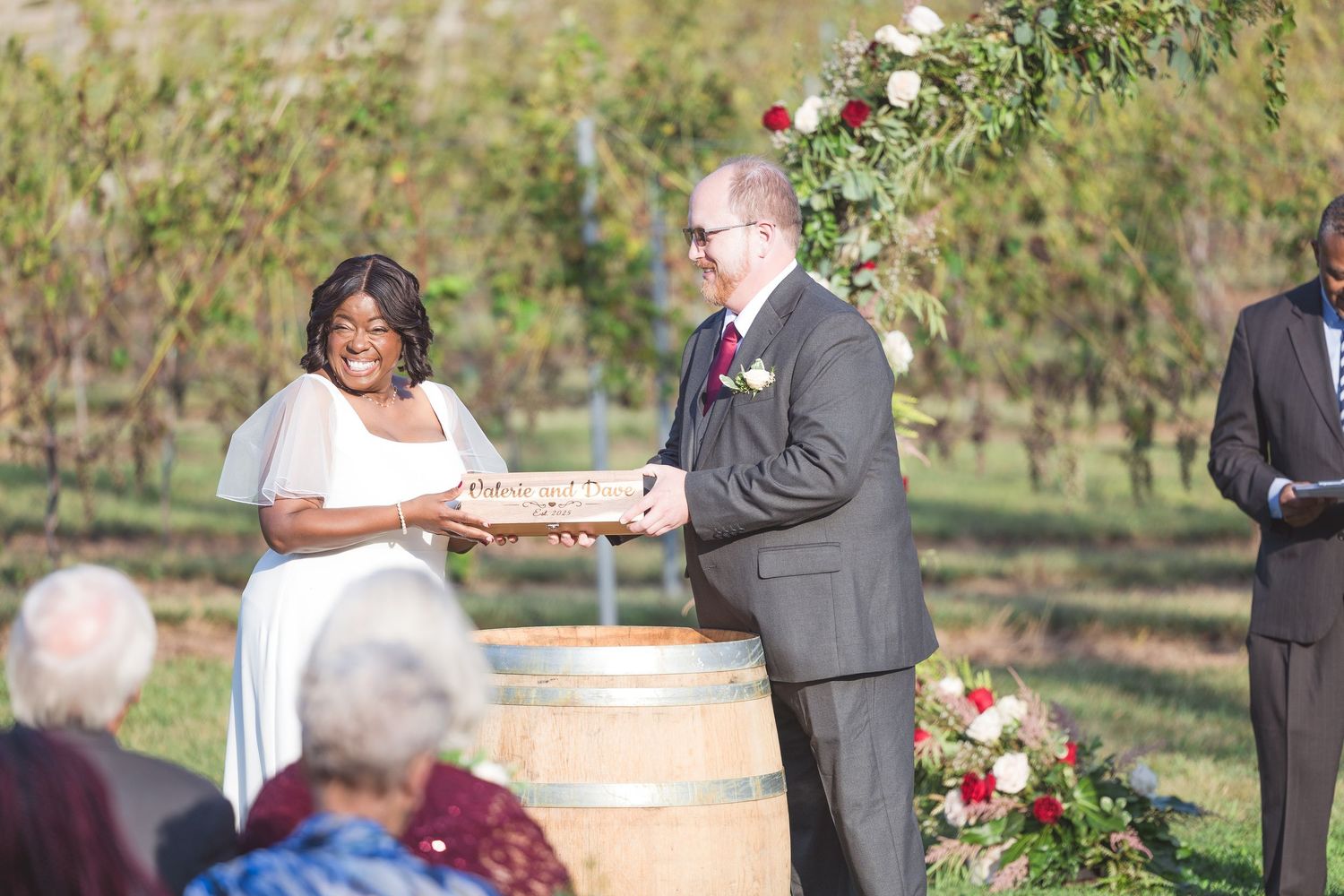 Outdoor wedding ceremony with wine barrels and floral arrangements in a vineyard setting.