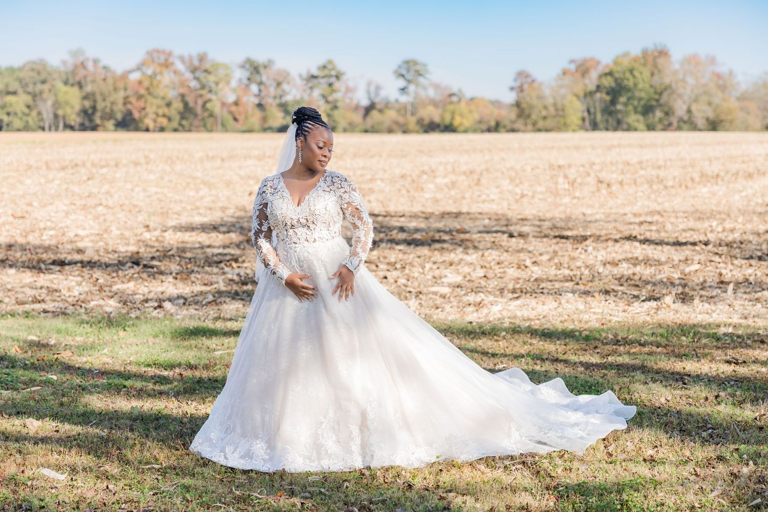 A bride in a flowing white wedding dress poses gracefully in a sun-drenched autumn field.