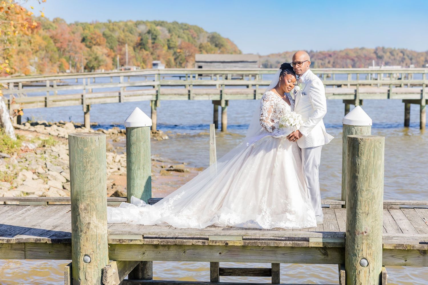 Scenic autumn dock wedding photos captured along a waterfront pier with fall foliage in the background.