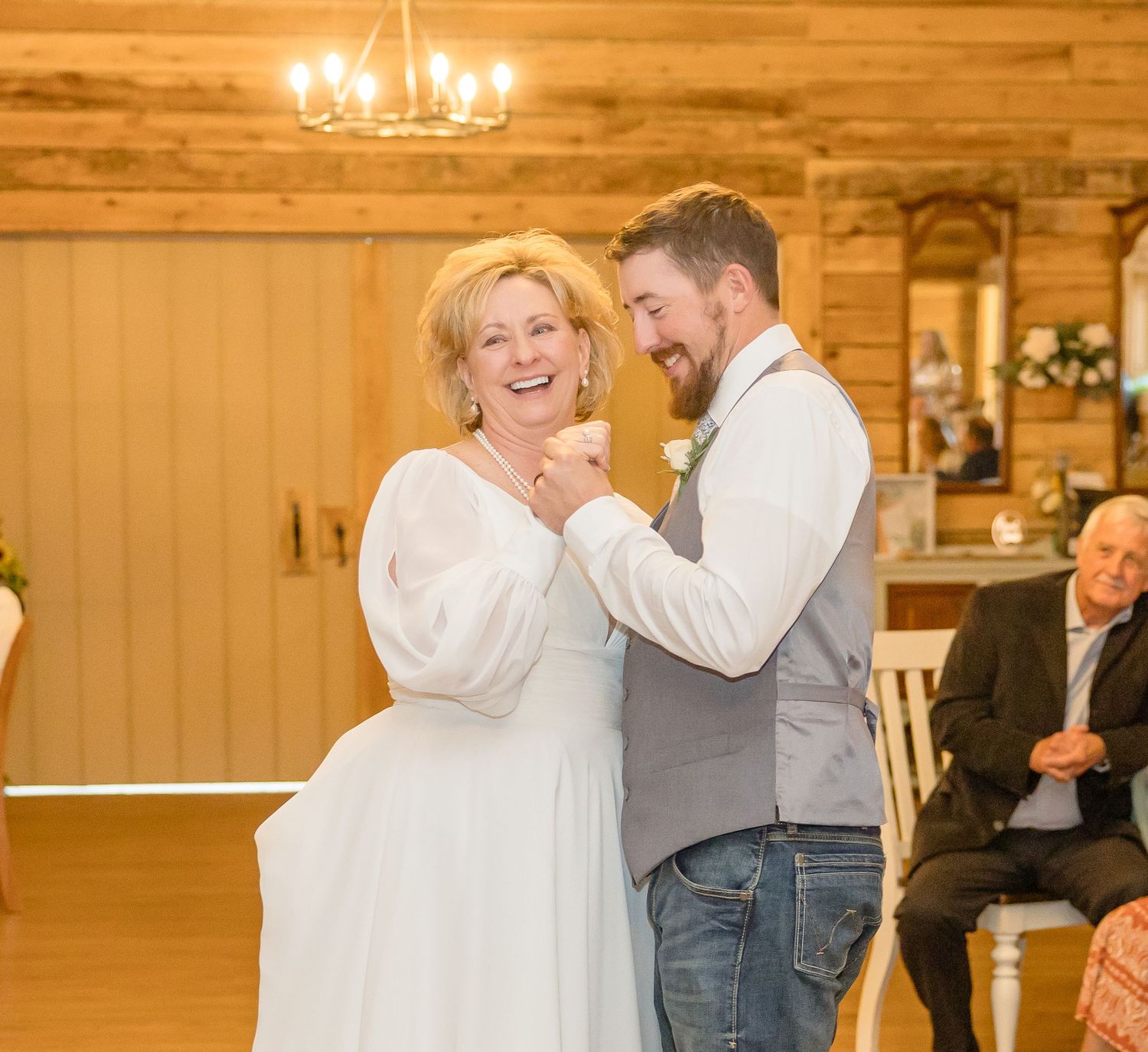 Couples dance together in a warmly lit rustic venue with chandeliers.