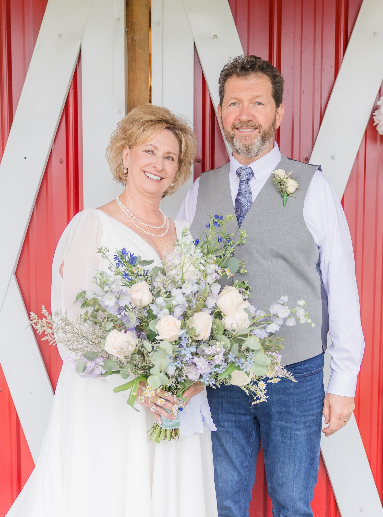 Wedding couple poses against red and white striped backdrop holding delicate floral bouquets.
