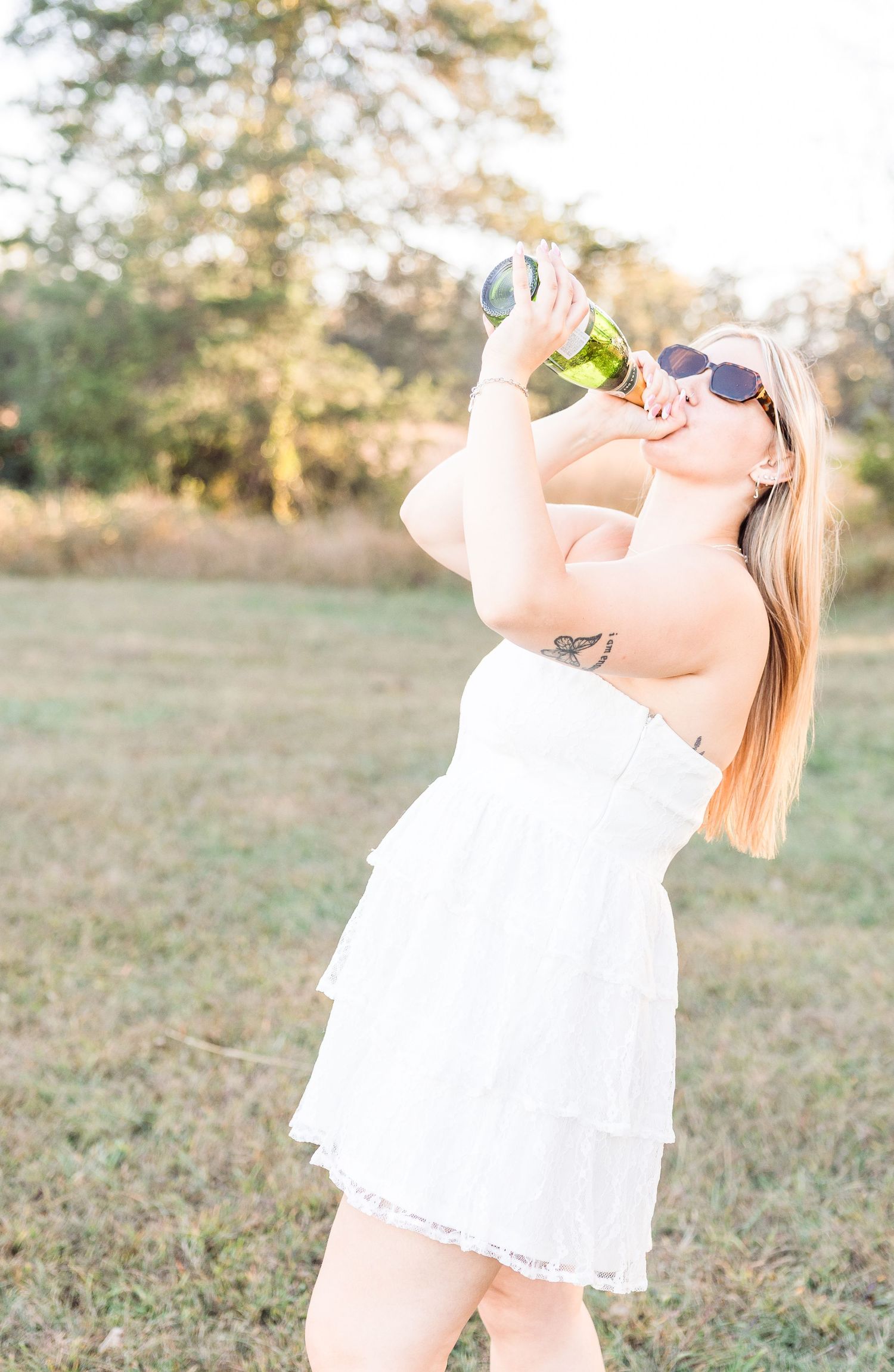 A person in white dress celebrates with champagne in an outdoor field.