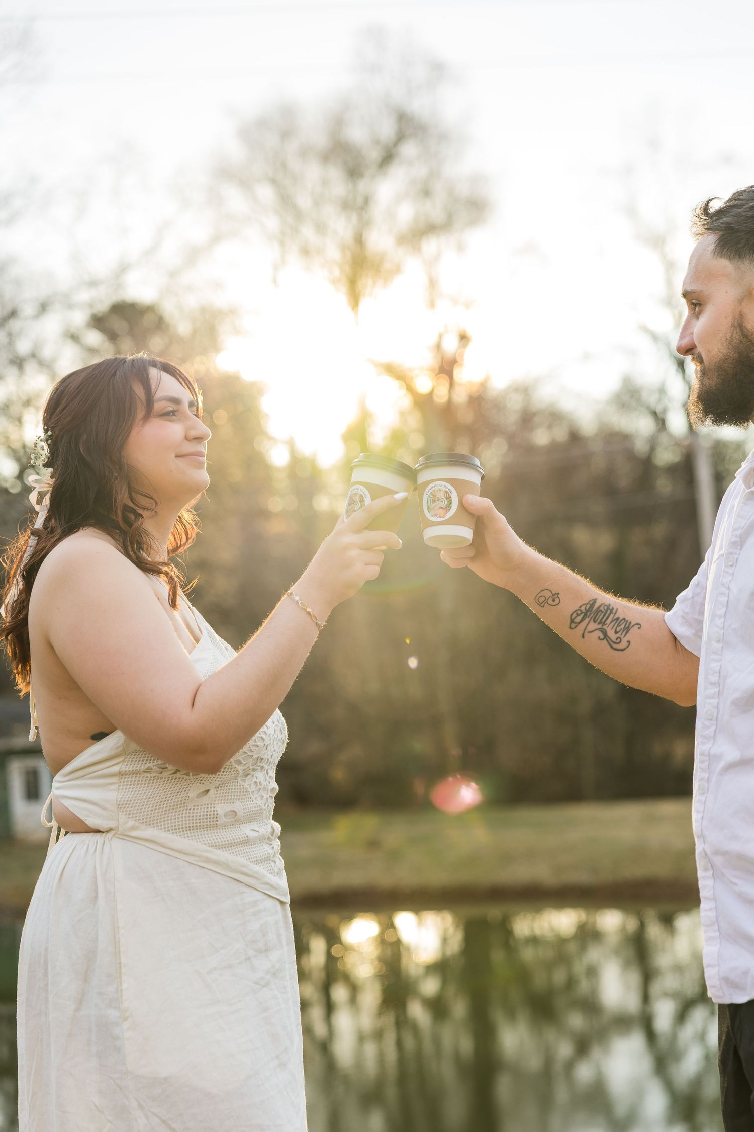 Couple shares playful moment blowing bubbles at sunset by a lake in romantic outdoor photoshoot.