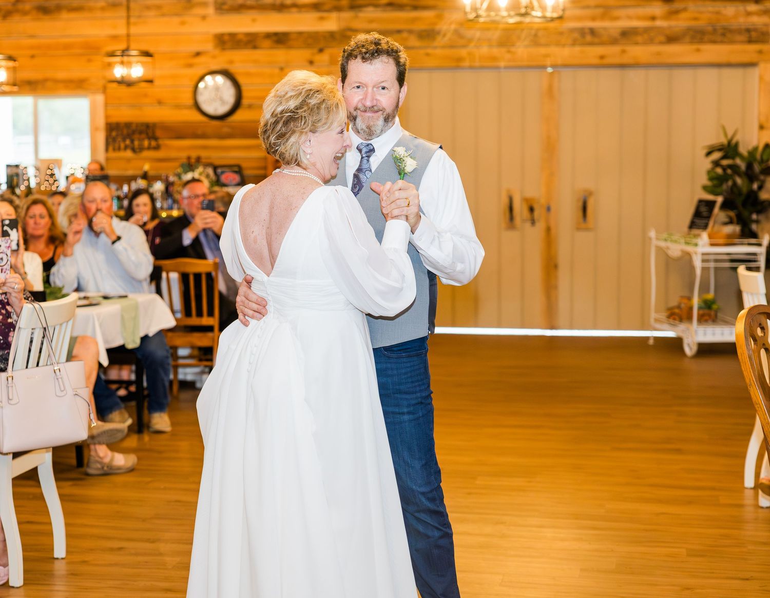 Wedding couples share first dances in warmly lit rustic barn reception venue.