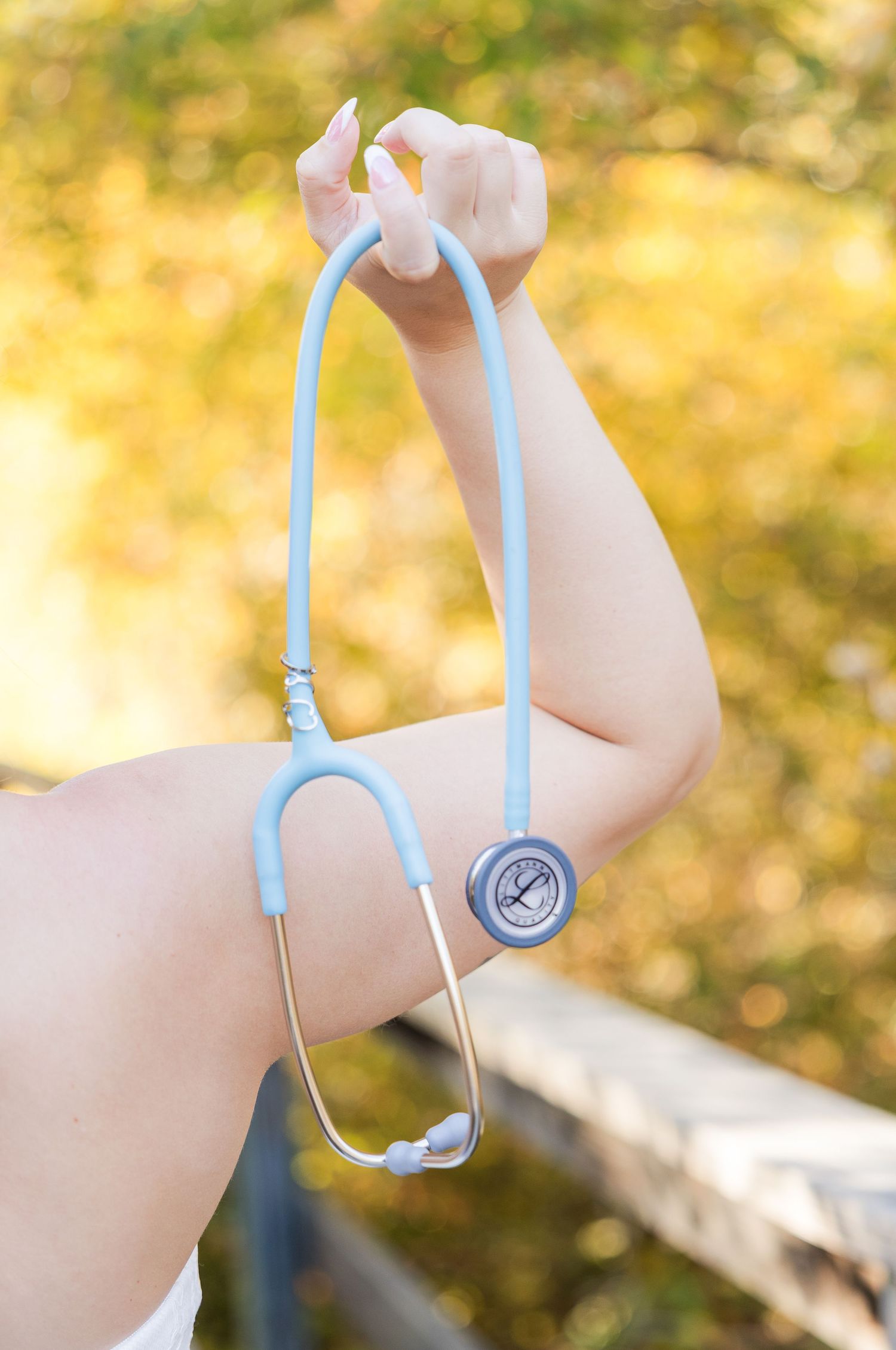 A light blue stethoscope held up against a warm golden background.