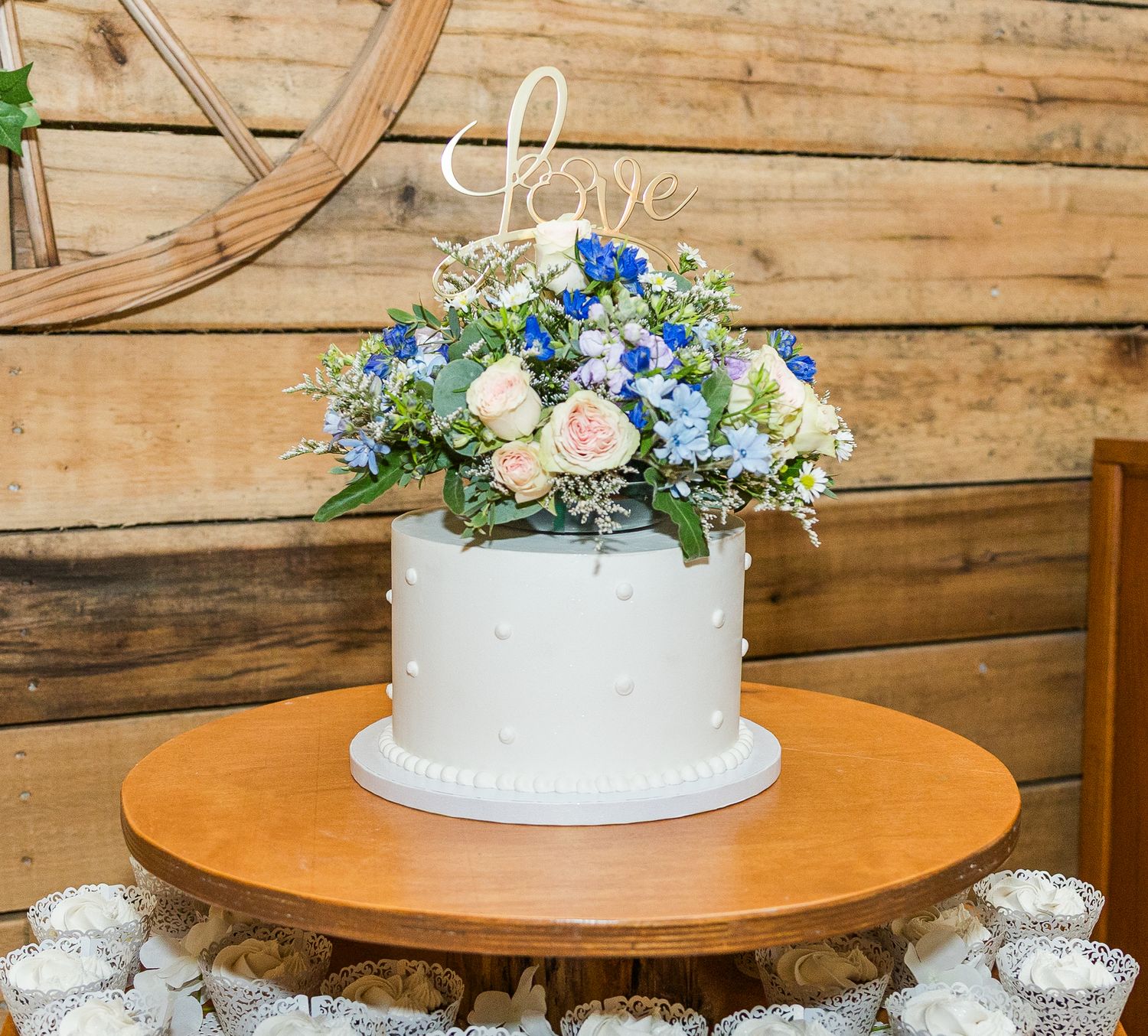 White wedding cake displayed on wooden table with blue and white floral decorations.