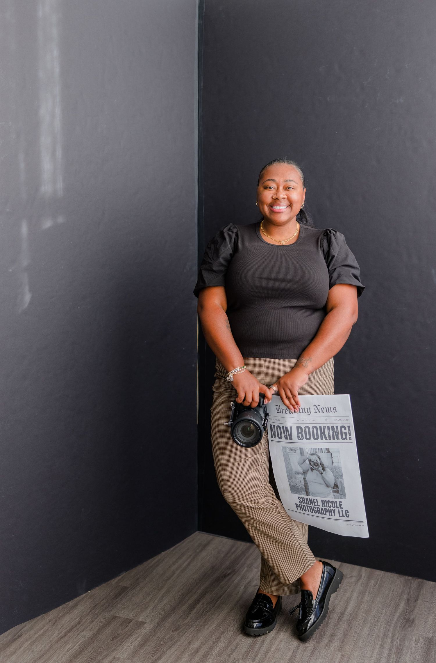 A person wearing a black shirt and khaki pants sits against a gray wall while holding printed materials.