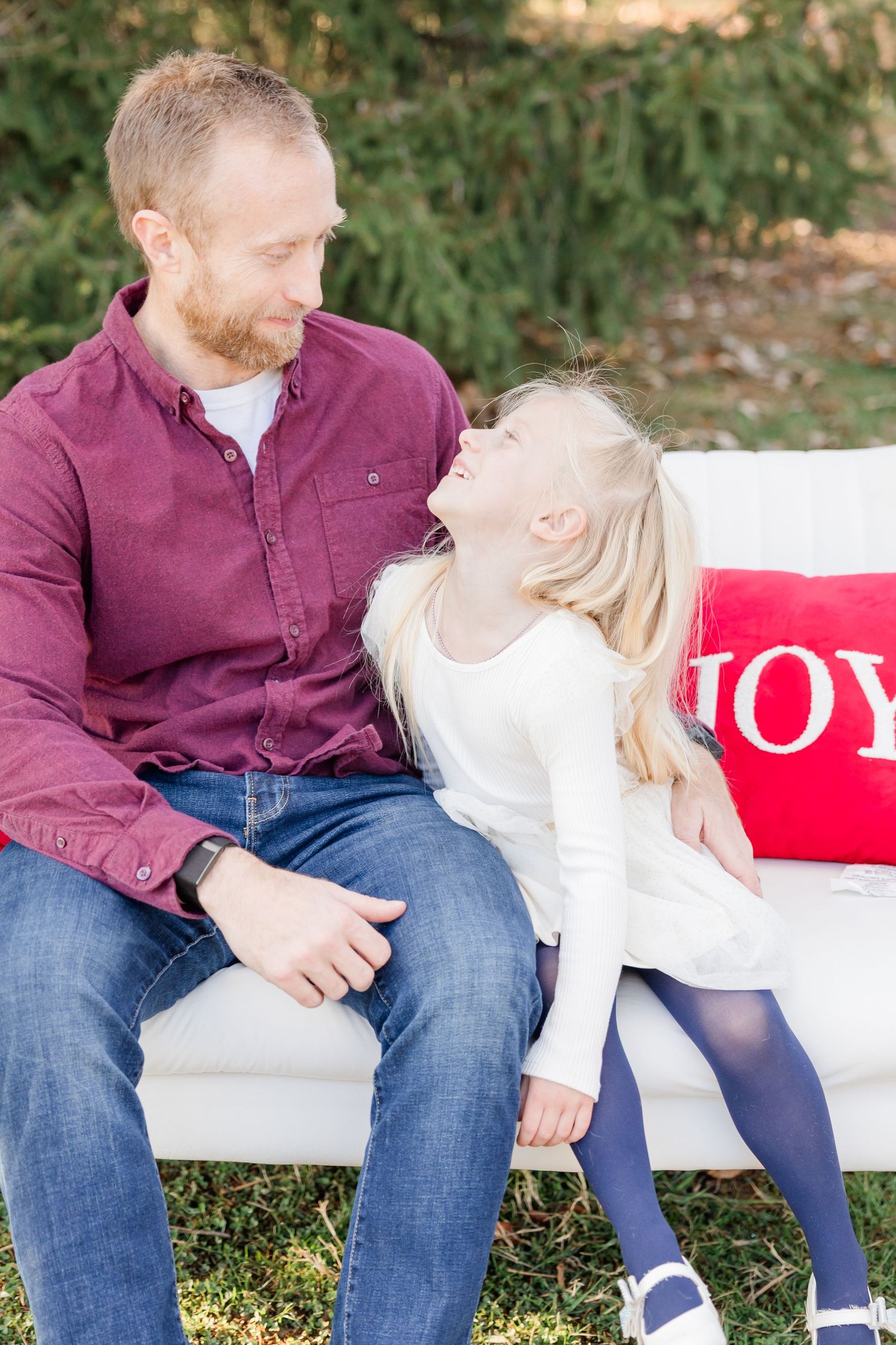Two people sitting close together on a white cushioned surface with decorative pillows outdoors.