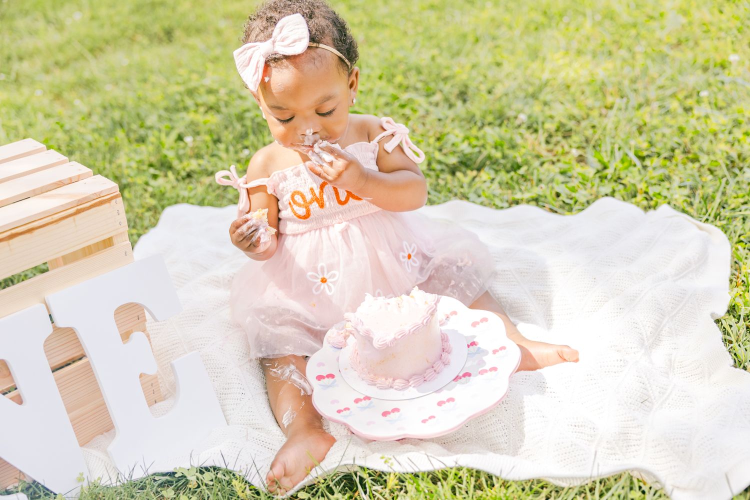 Baby in pink dress crawls on white blanket during outdoor photo session.