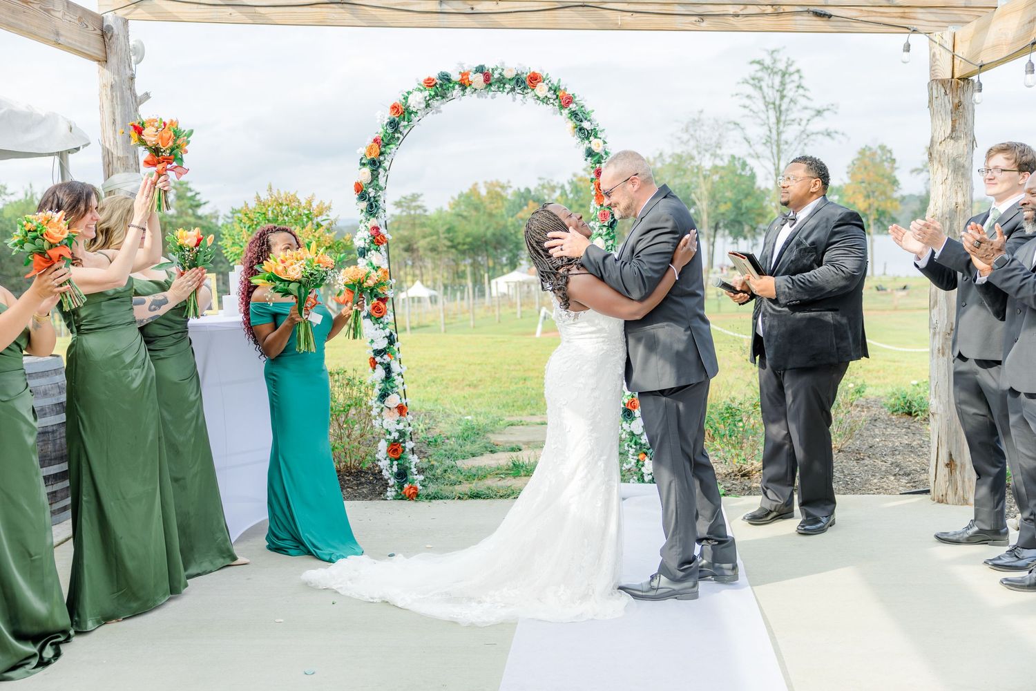Wedding ceremony with bridal party in emerald green dresses watching the couple's first kiss.