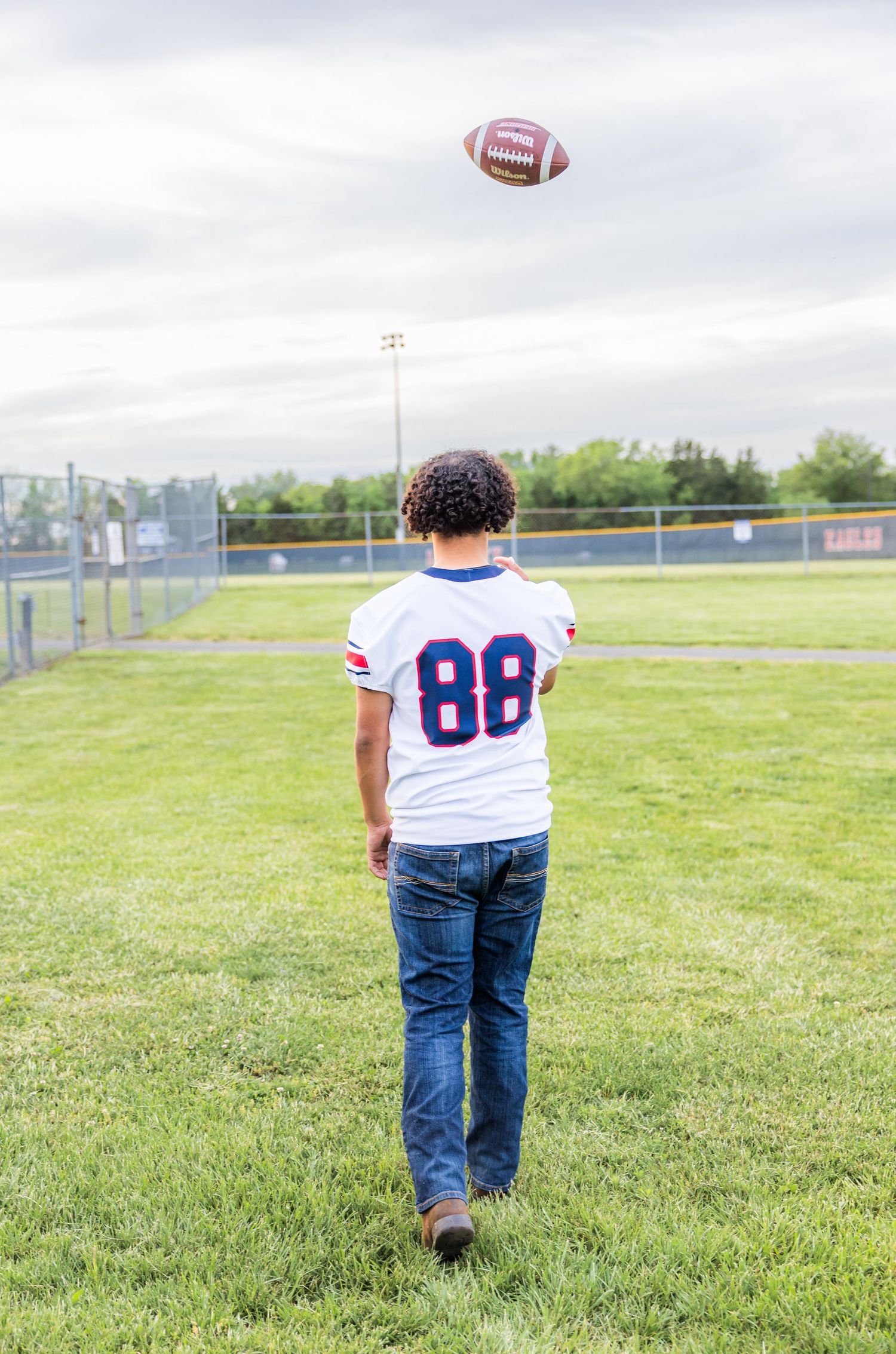 A football player in jersey number 88 stands on a field watching a football soar through the air.