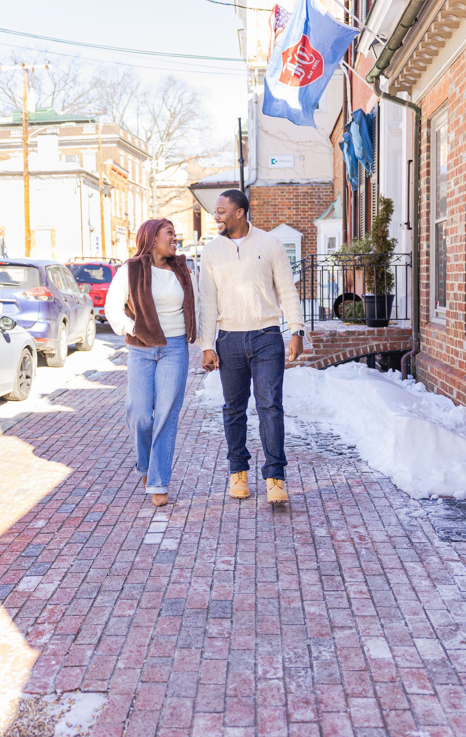 Couple walking together on a brick pathway with snow on the ground on a sunny winter day.