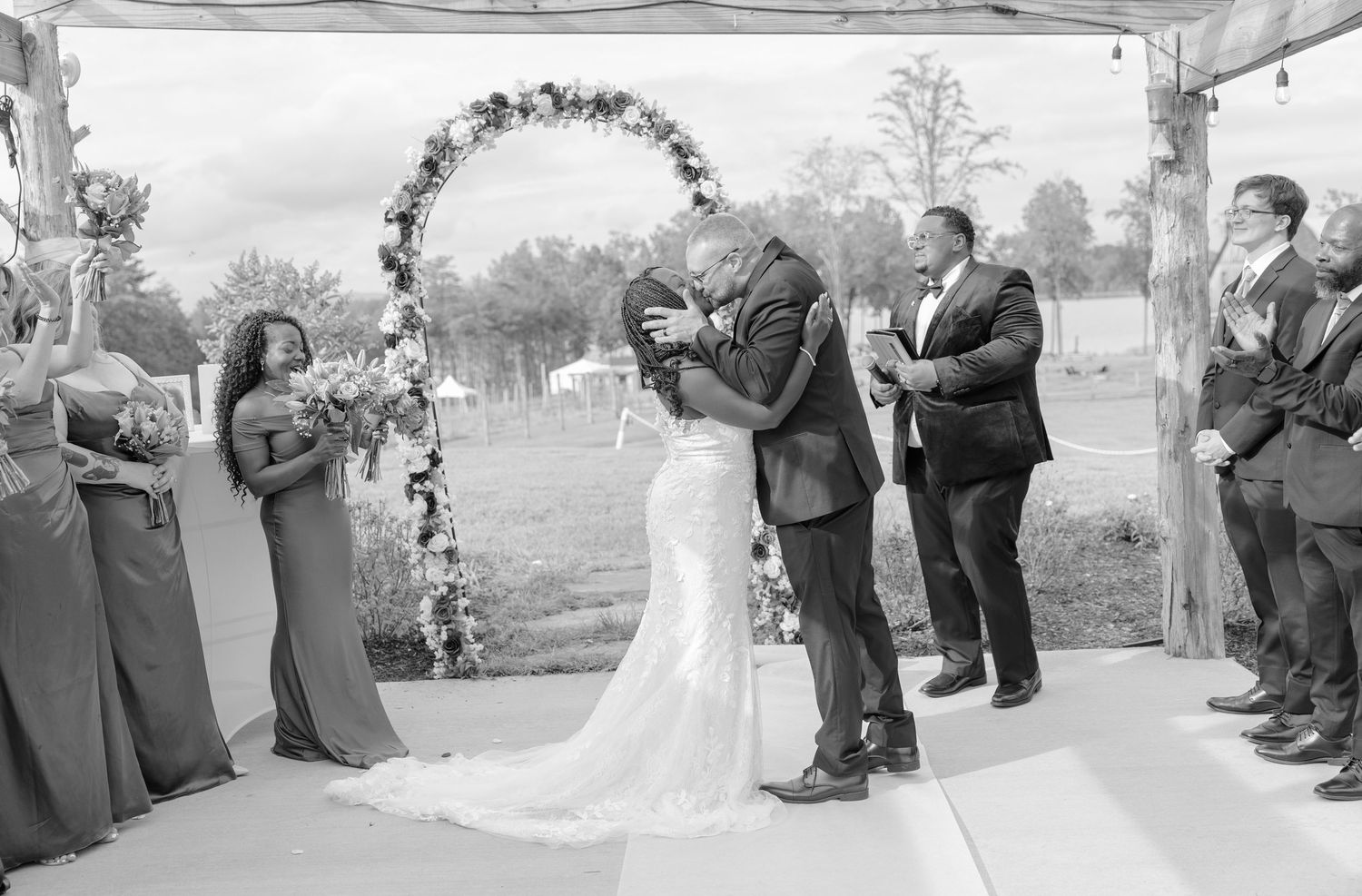 Black and white wedding photo showing wedding party and guests during the ceremony kiss.