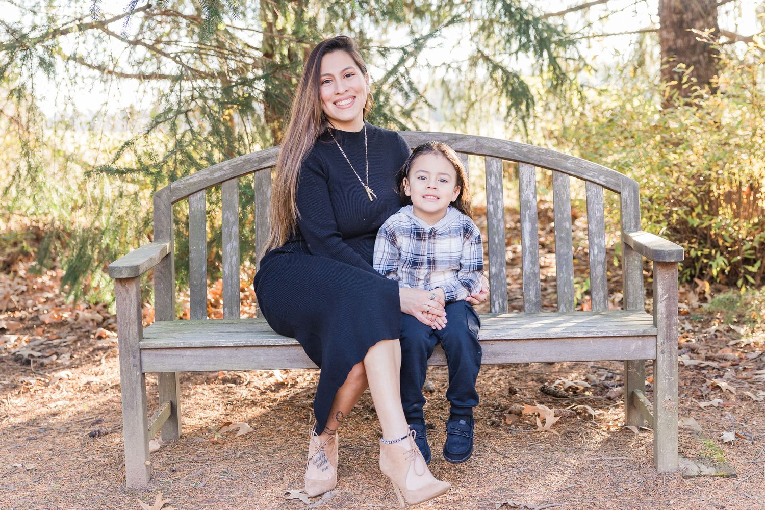 A family sits together on a wooden garden bench in a scenic outdoor setting during golden hour lighting.