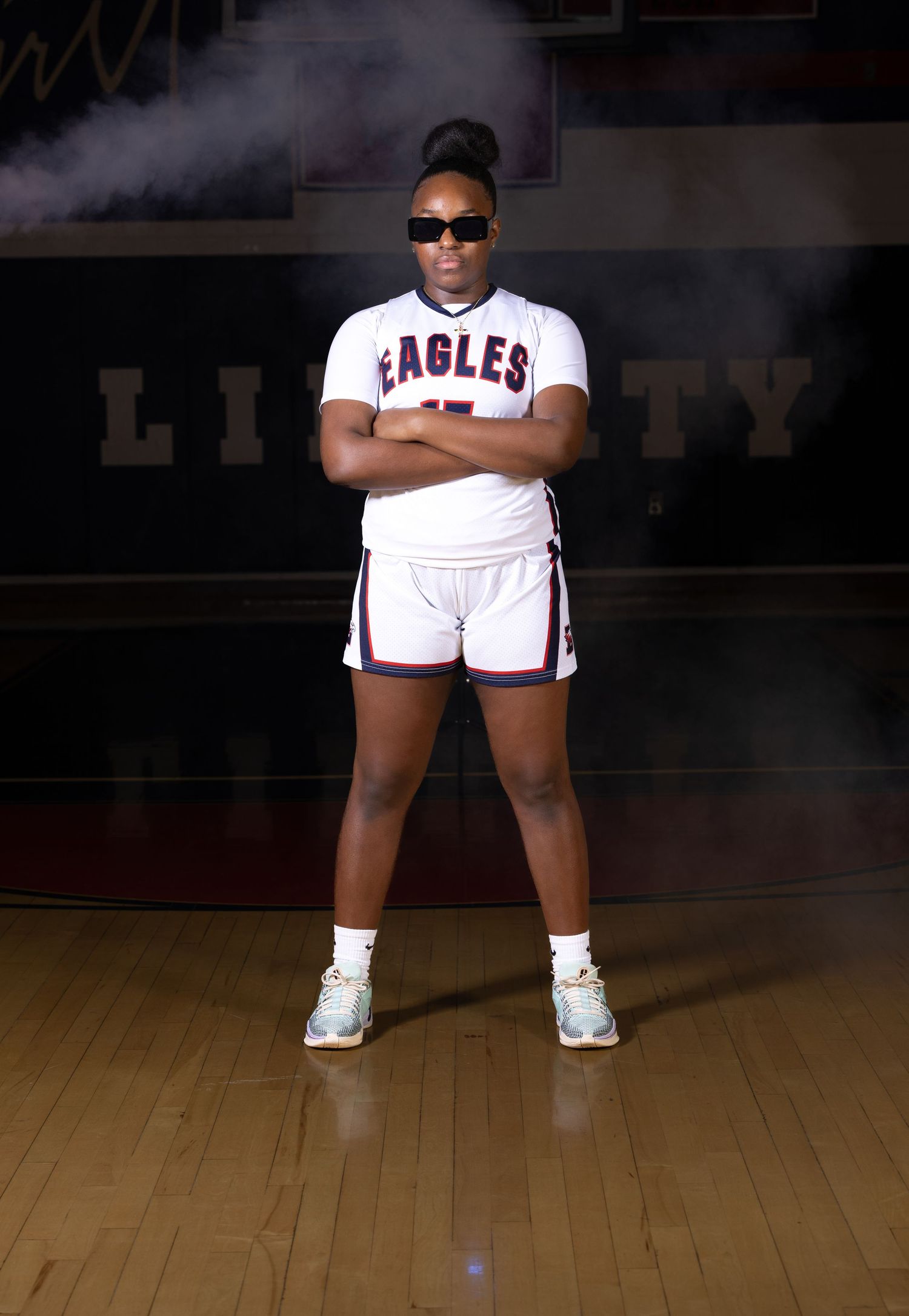 Basketball player in Eagles uniform poses on court with dramatic lighting.