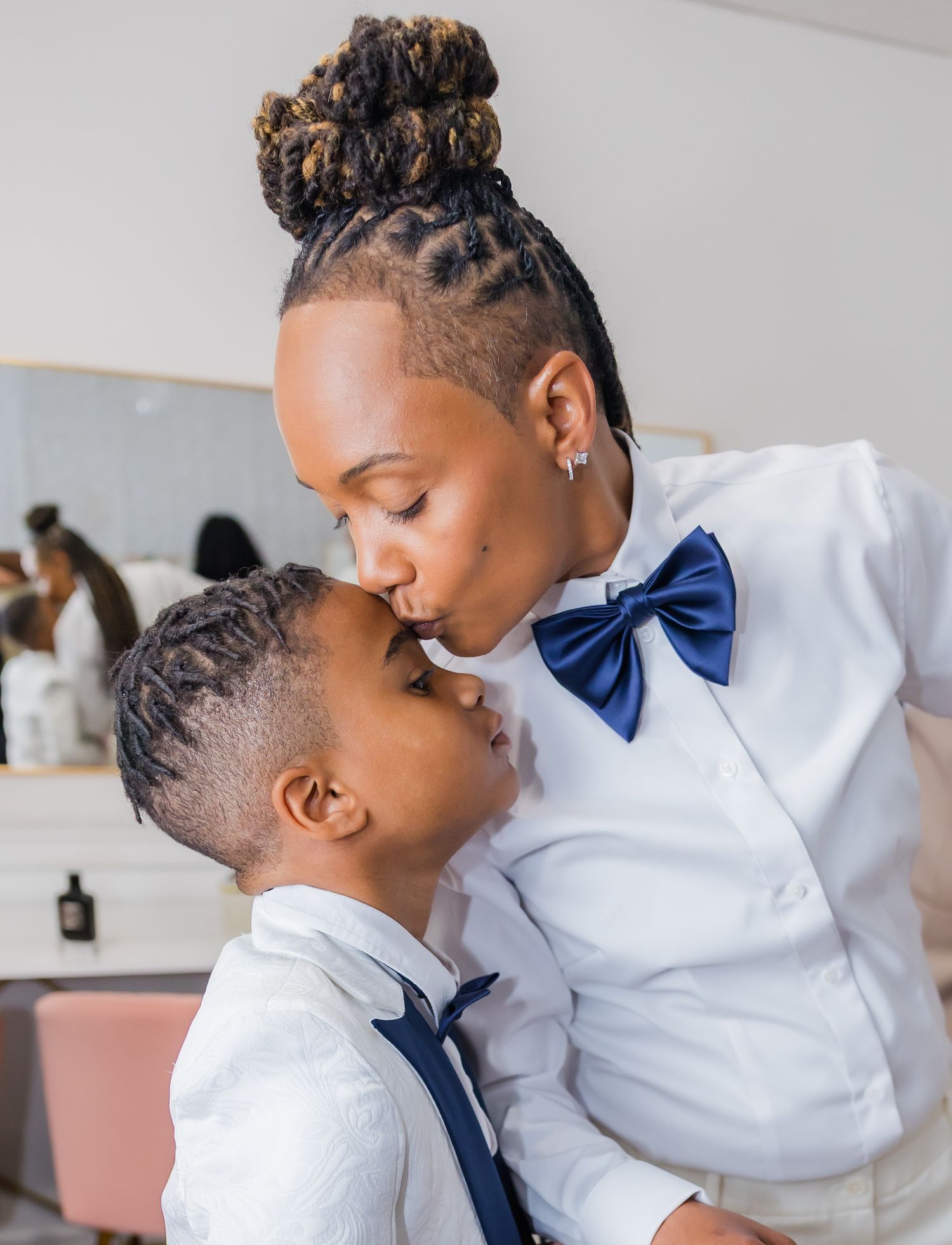A tender moment shared between two people in formal attire with one wearing a white suit and navy vest.