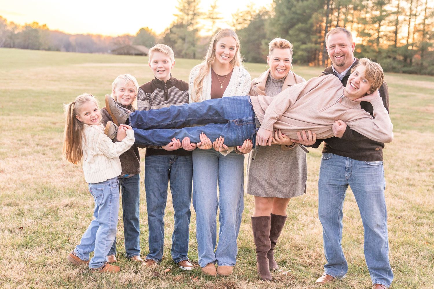 Group of people wearing denim and brown clothing pose together in a field at sunset.