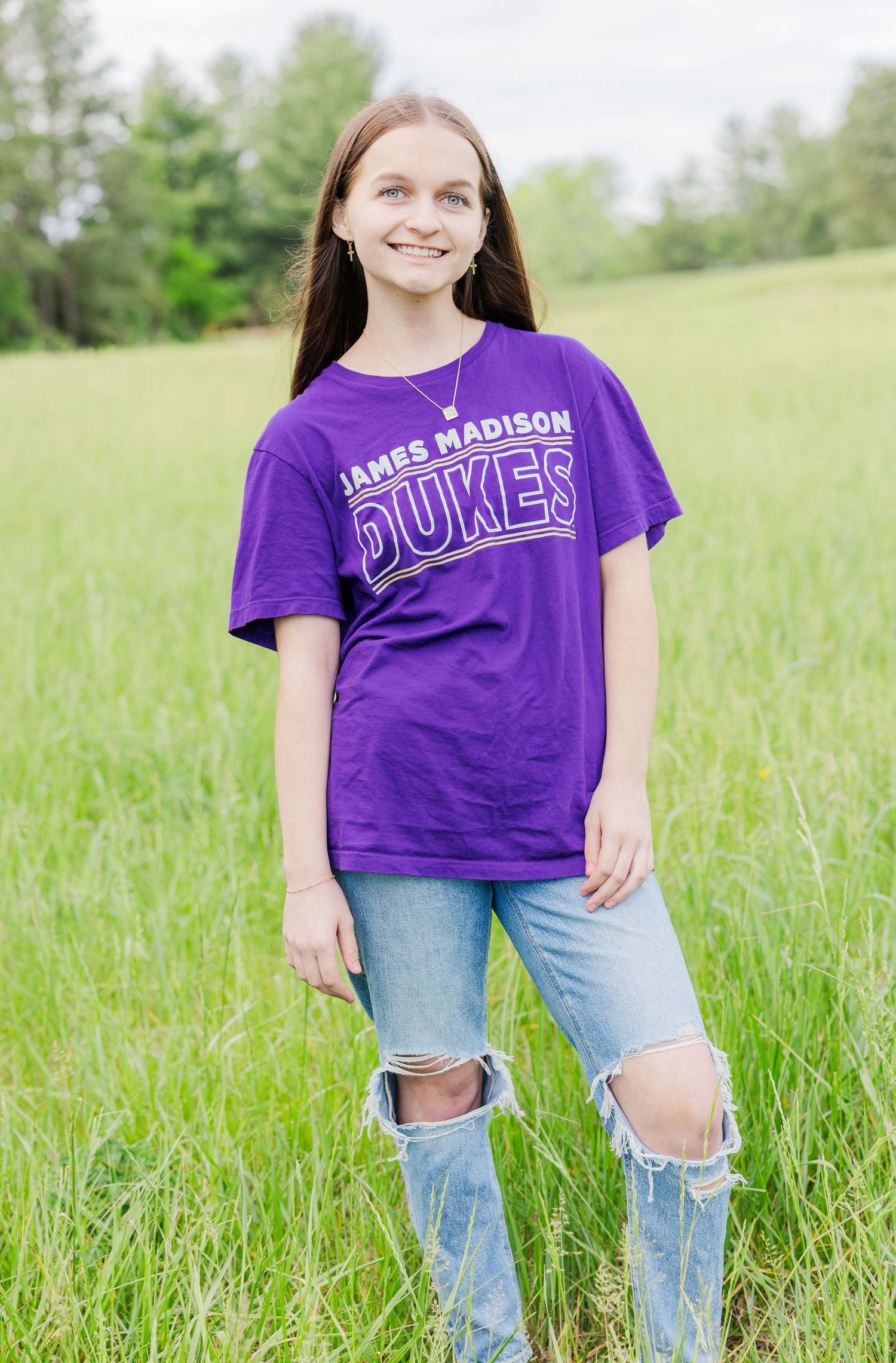 Casual portraits in a grassy field wearing purple university shirt and ripped jeans.