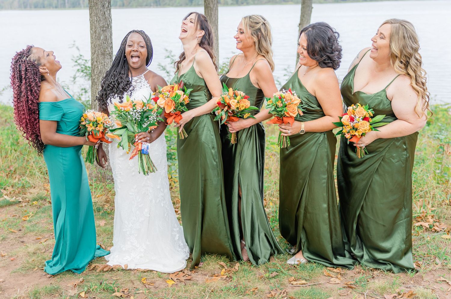 Bridesmaids in emerald green dresses hold orange bouquets while standing together outdoors.