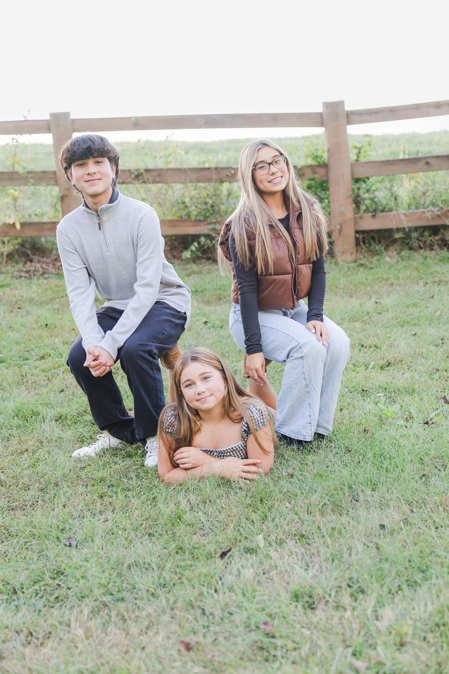 Three casual outdoor portraits showing people relaxing and posing together on grassy ground with a wooden fence in background.
