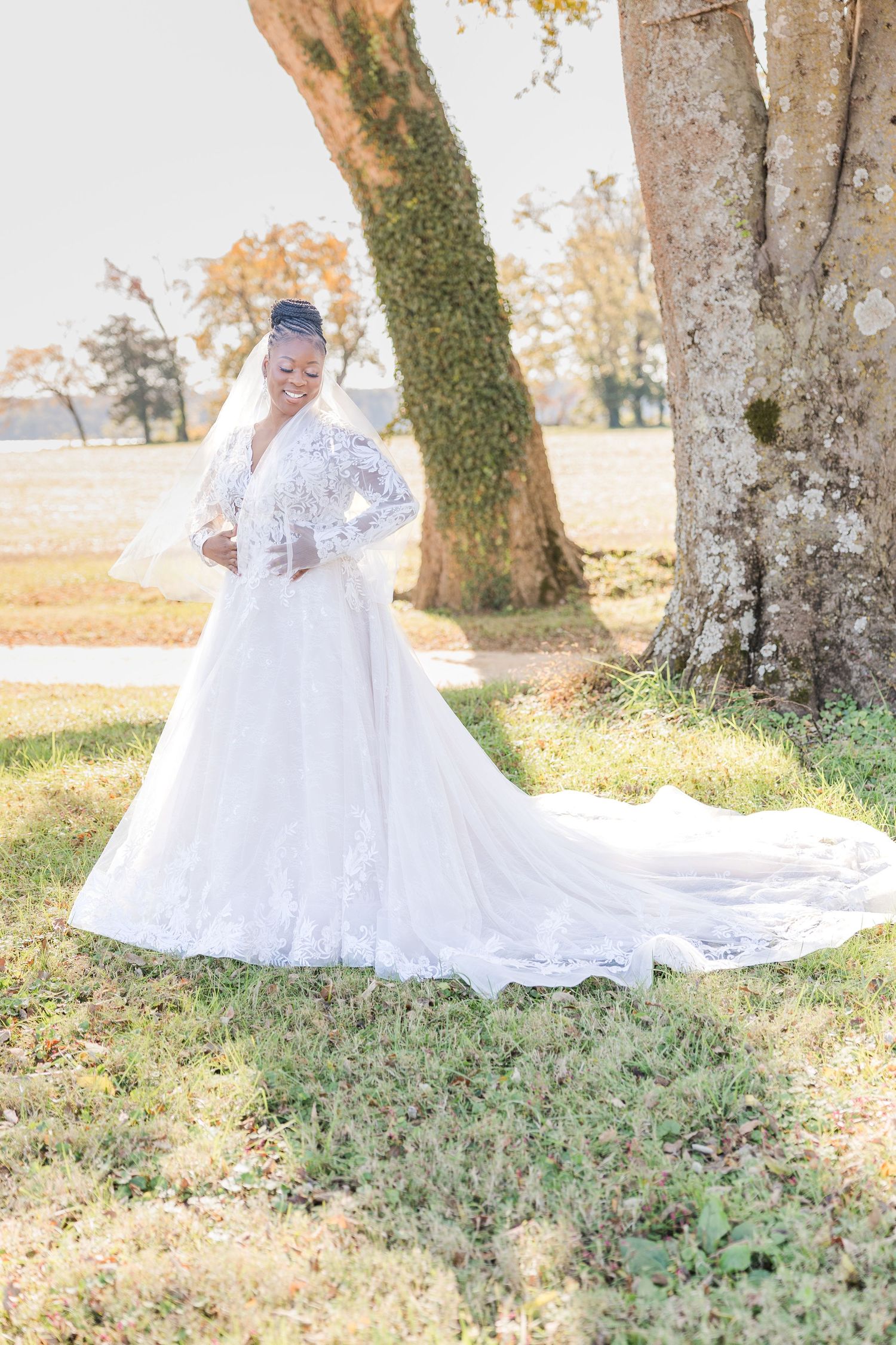 A white lace wedding dress with long train flows elegantly across mossy ground beneath autumn trees.