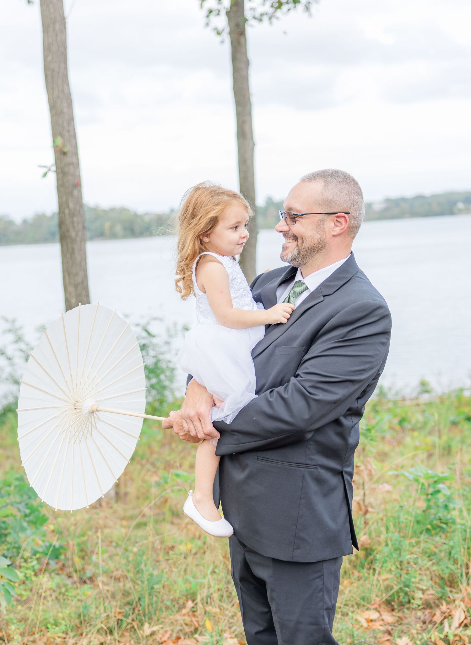 Couple poses with parasol by lakeside during outdoor photo session in natural setting.