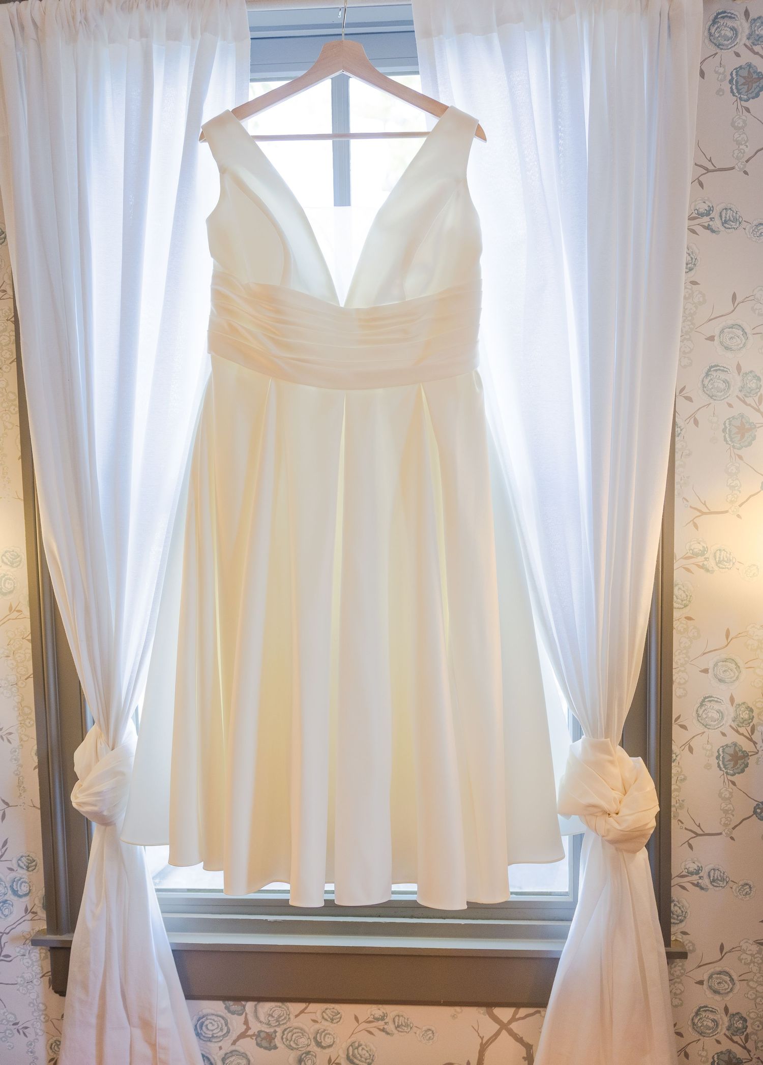 White wedding dresses and bridesmaid gowns hanging on display in a sunlit dressing room.