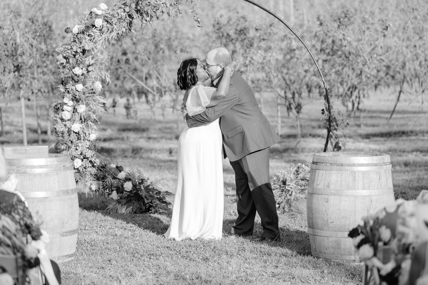 A black and white photo of wedding guests gathered around wooden barrels outdoors.