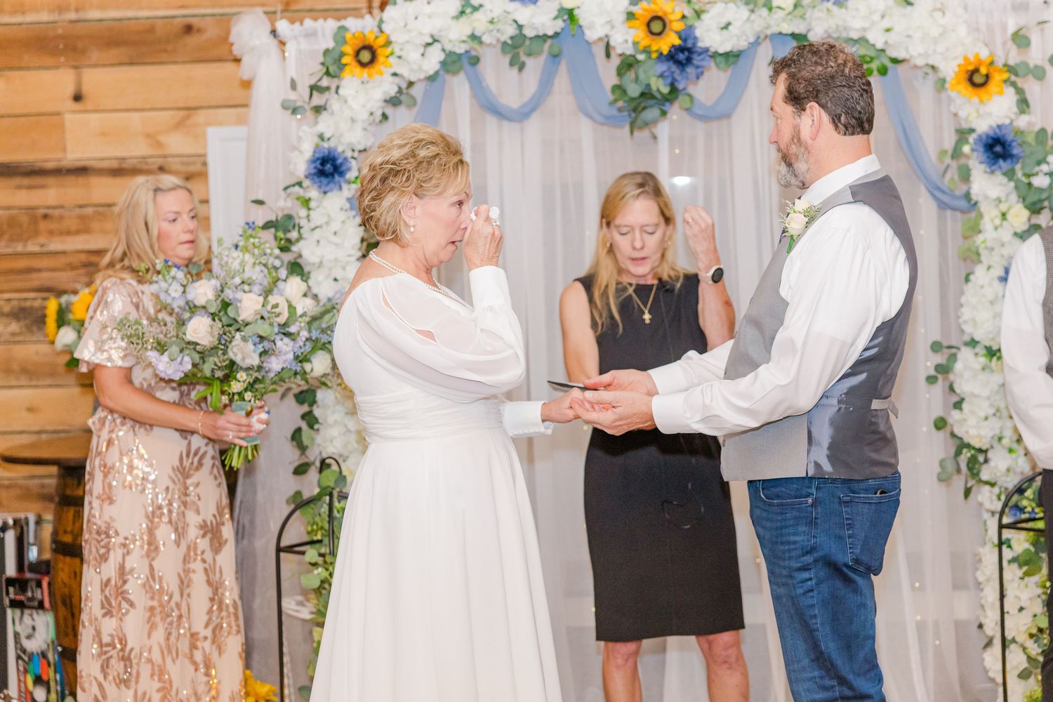 Wedding guests dance and celebrate at a rustic barn venue decorated with sunflowers and white floral arrangements.