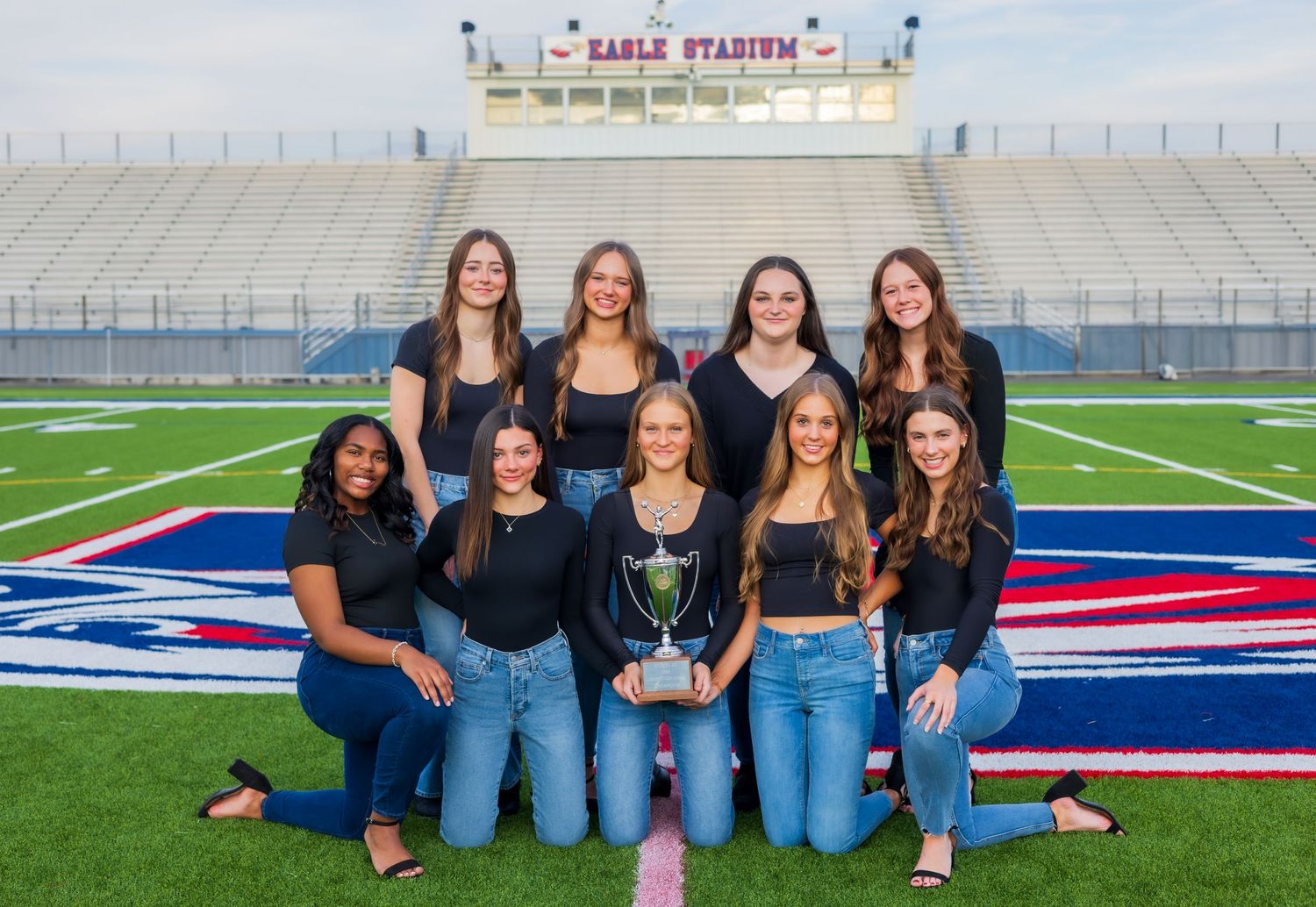 Group photo of cheerleaders in matching jeans and black tops posing on a football field.