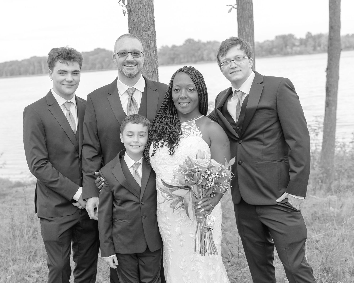 Groomsmen in black suits pose casually outdoors for wedding photos.