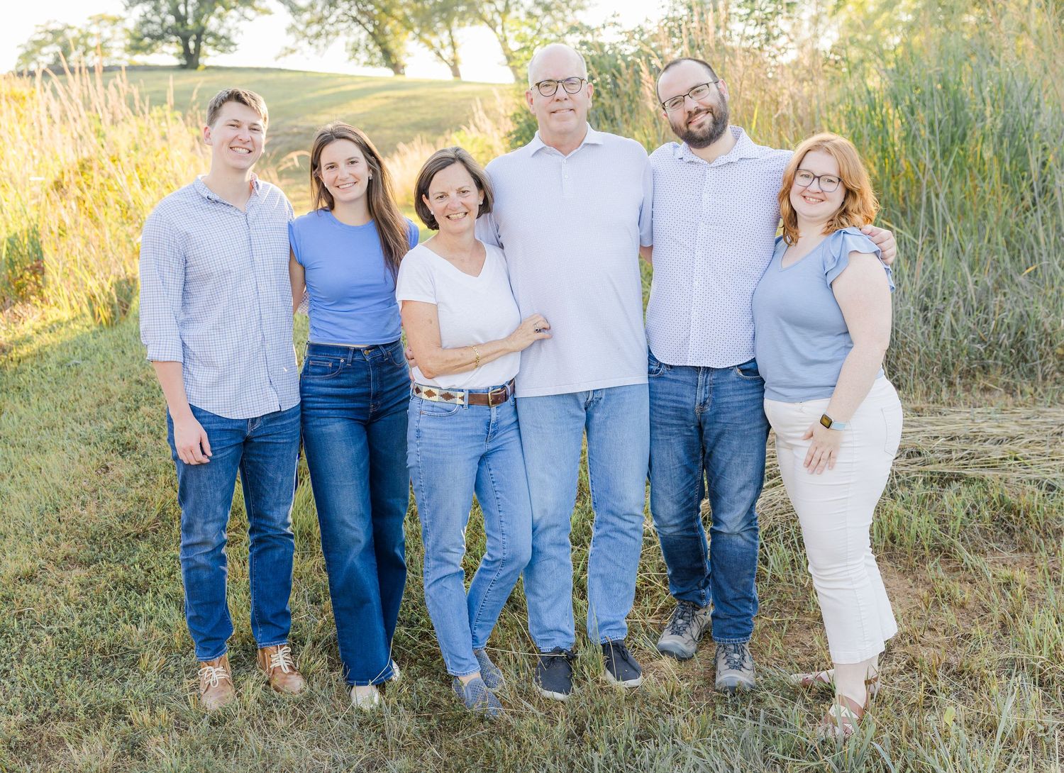 A casual group photo taken in front of tall grass during sunset.