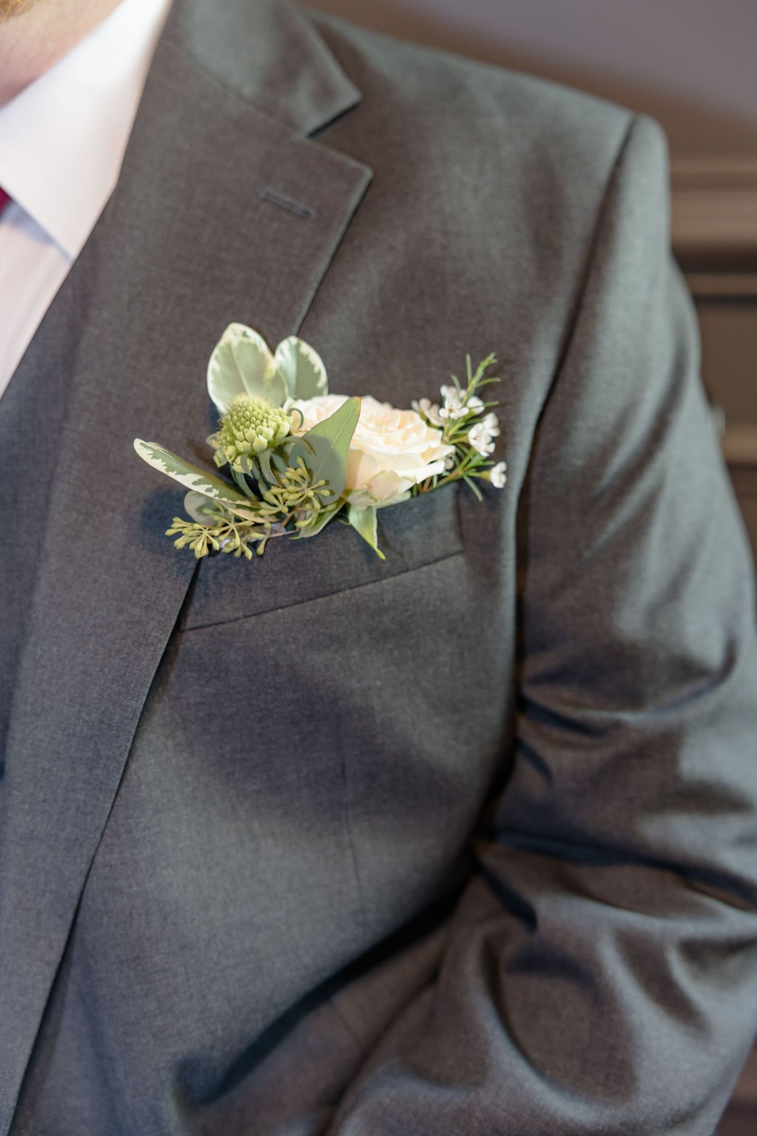 Elegant white and green floral boutonniere pinned to a charcoal gray suit jacket.